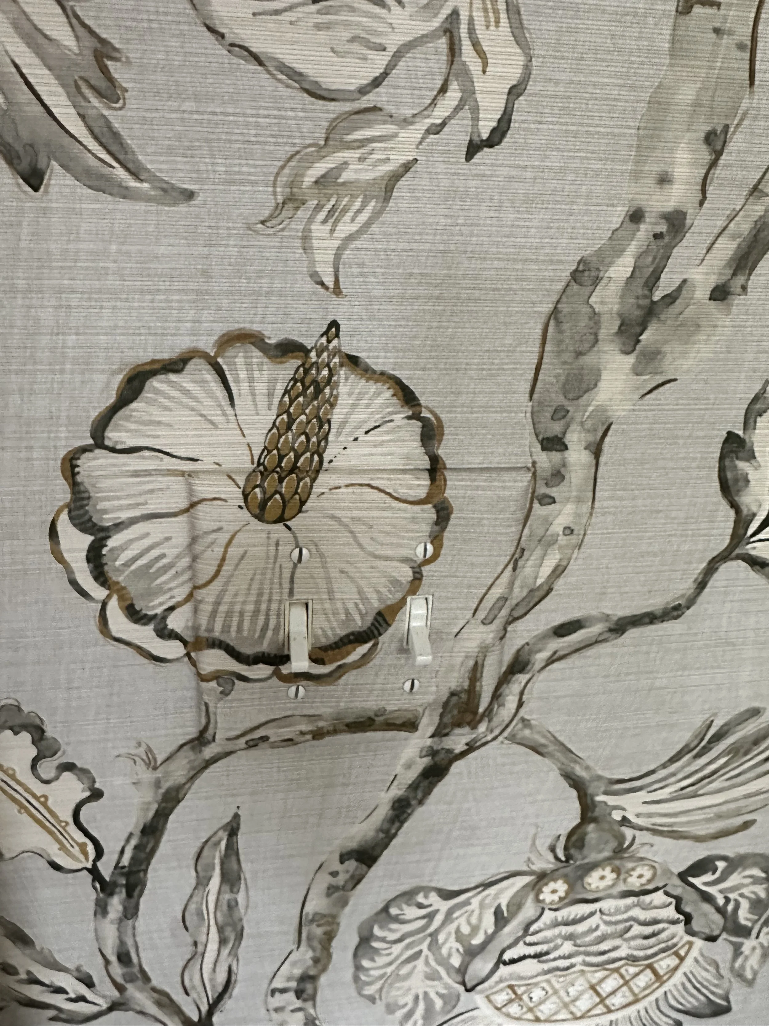 Close-up of a decorative fabric with a botanical pattern featuring large flowers, leaves, and a branch, in shades of gray, black, and beige.
