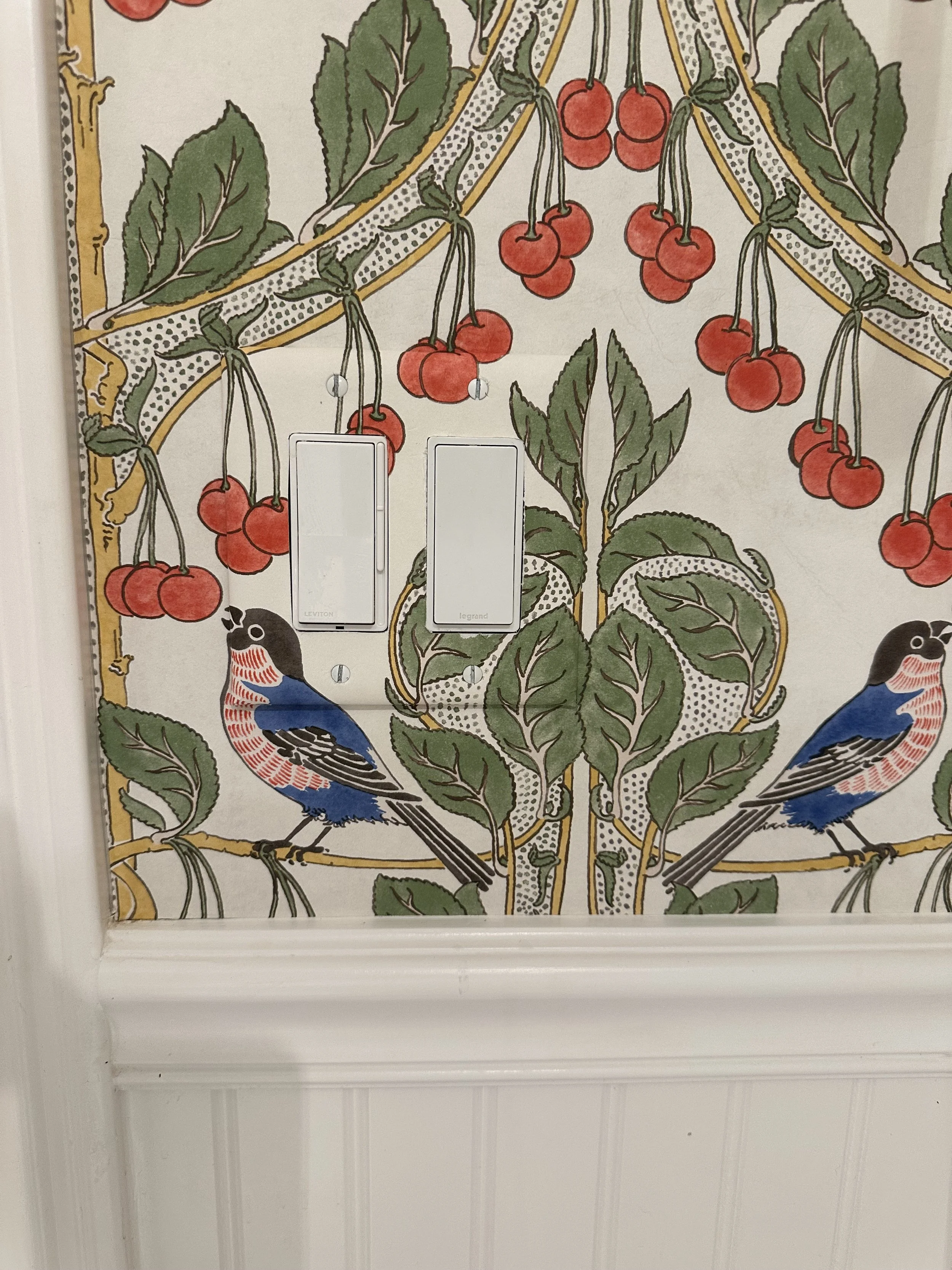Decorative wallpaper with birds, leaves, and cherries, and two white switch plates.