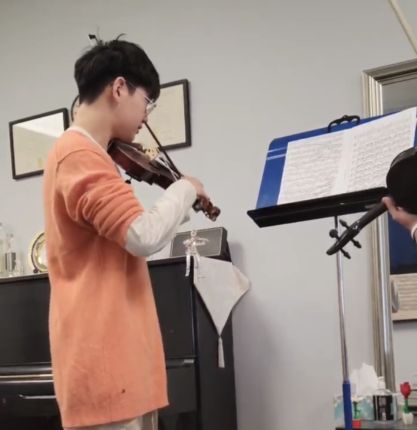 Young boy playing violin in a room with music stand and sheet music.