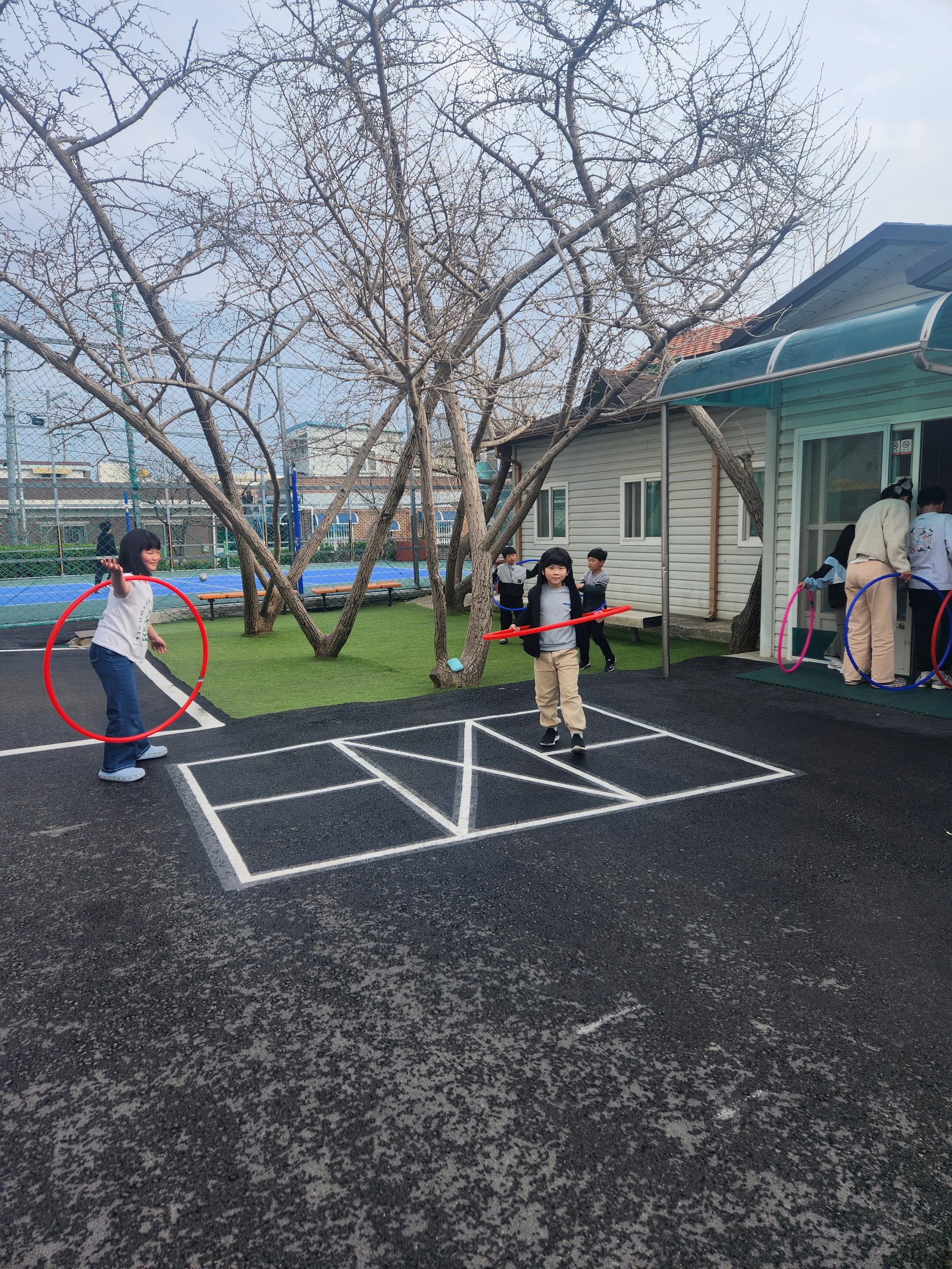 Children playing with hoops on a playground with outdoor sports courts and leafless trees.