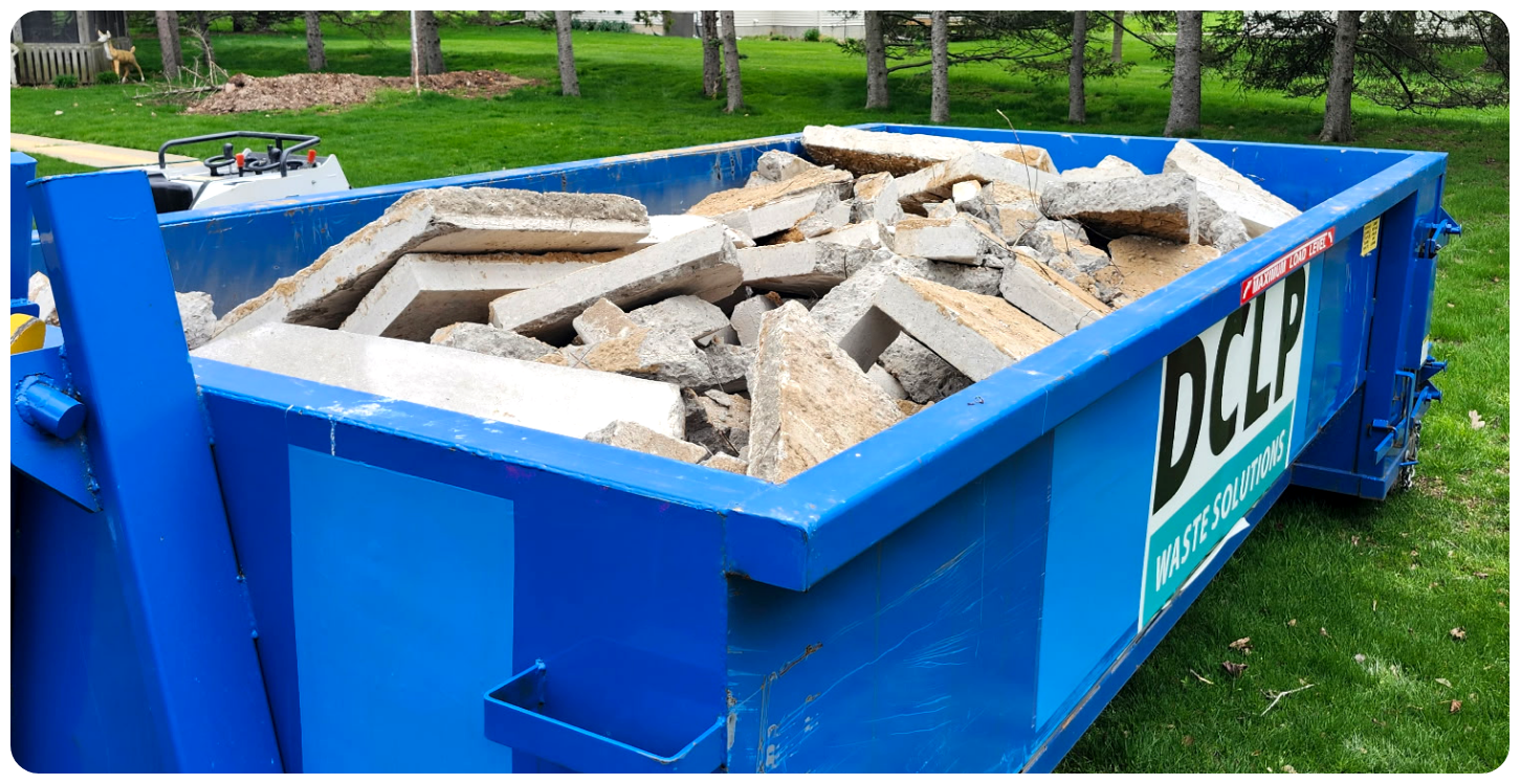Roll-off bin filled with concrete and construction debris for disposal.