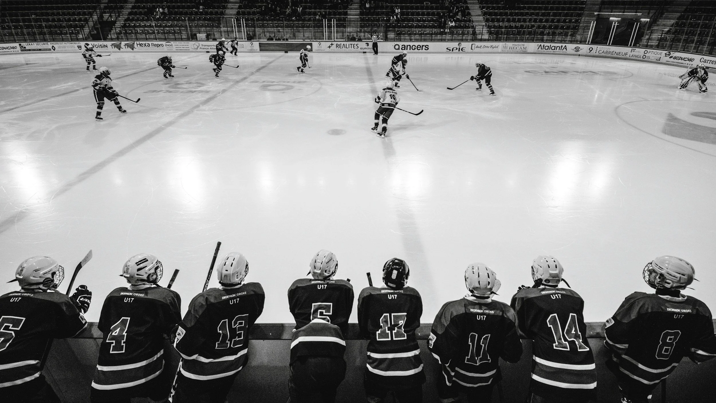 Hockey players on the ice during a game, with players on the bench at the forefront, all in black and white.