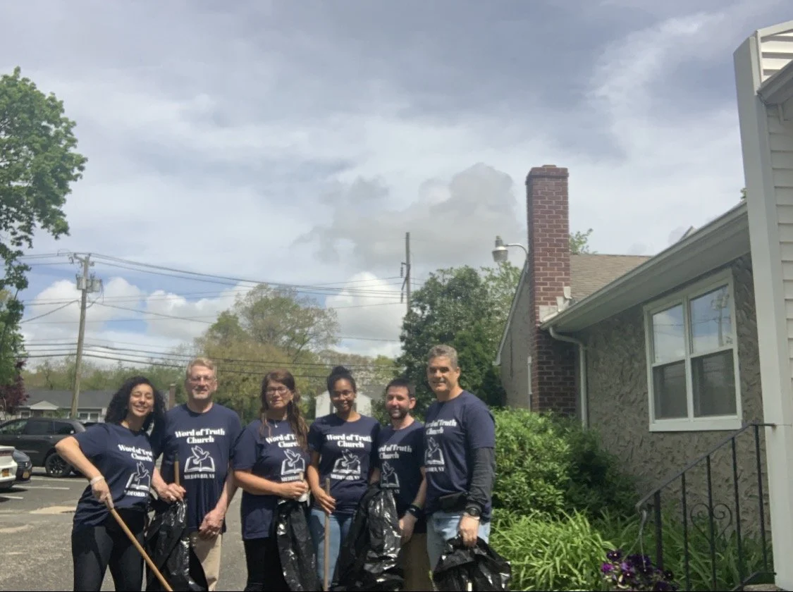 A group of six people wearing matching 'Word of Truth Church' T-shirts, standing outdoors with trash bags, participating in a community cleanup on a sunny day.