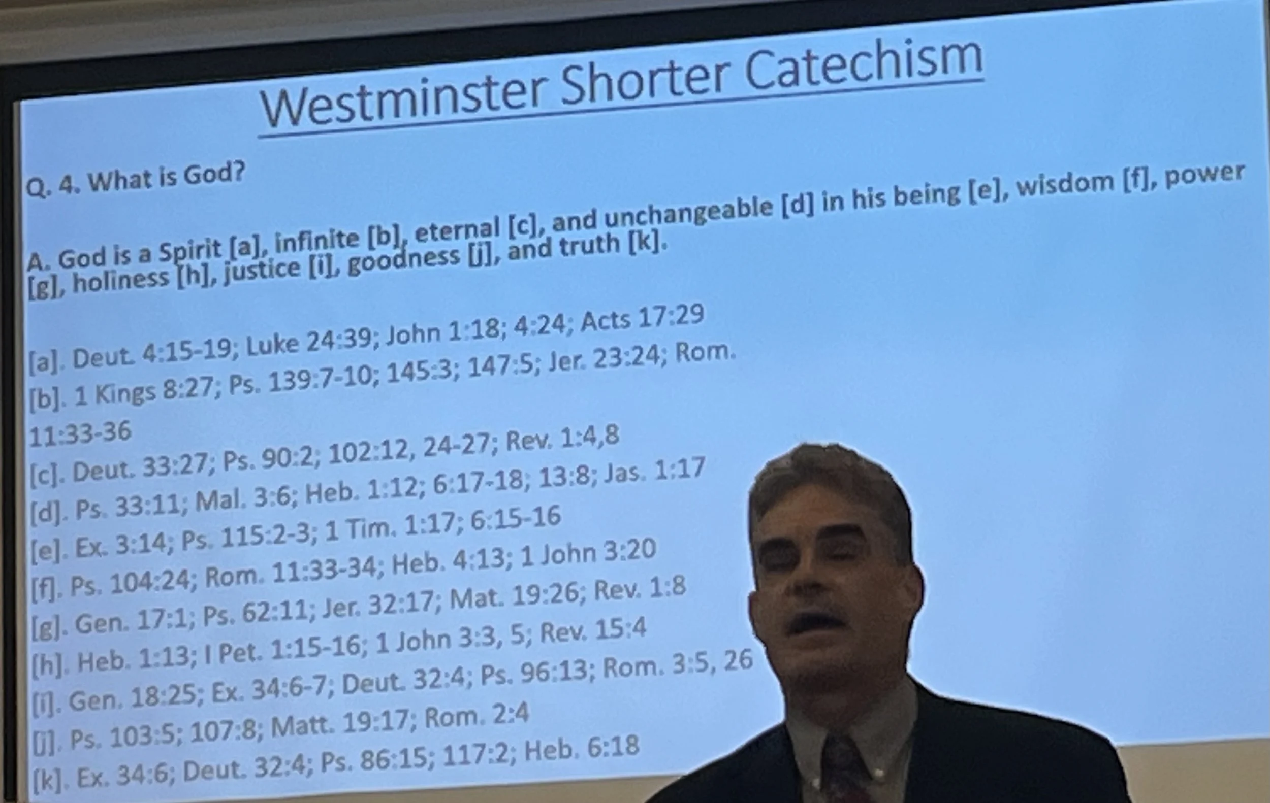 A presentation slide titled 'Westminster Shorter Catechism' with a person standing in front of it, partially obscuring the lower part of the slide.