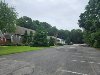 An empty parking lot with a row of residential buildings and green trees in the background.