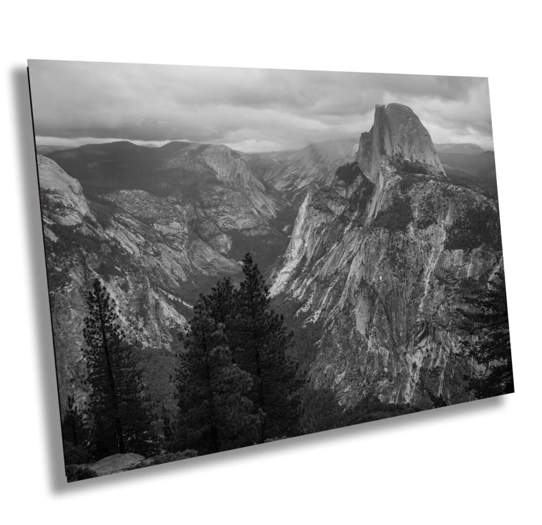 Black and white photograph of a mountain landscape, featuring a prominent large granite peak and surrounding forested area.