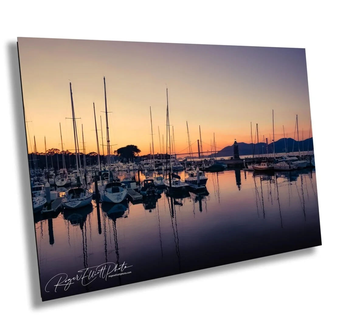 Sailboats and yachts docked at a marina during sunset with mountain silhouettes in the background.