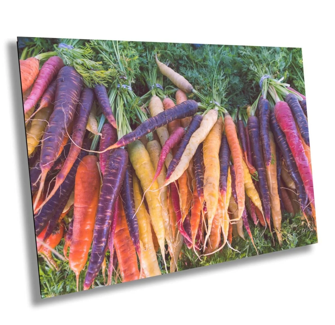 A variety of multicolored carrots, including purple, yellow, orange, and red, displayed on green leafy foliage.