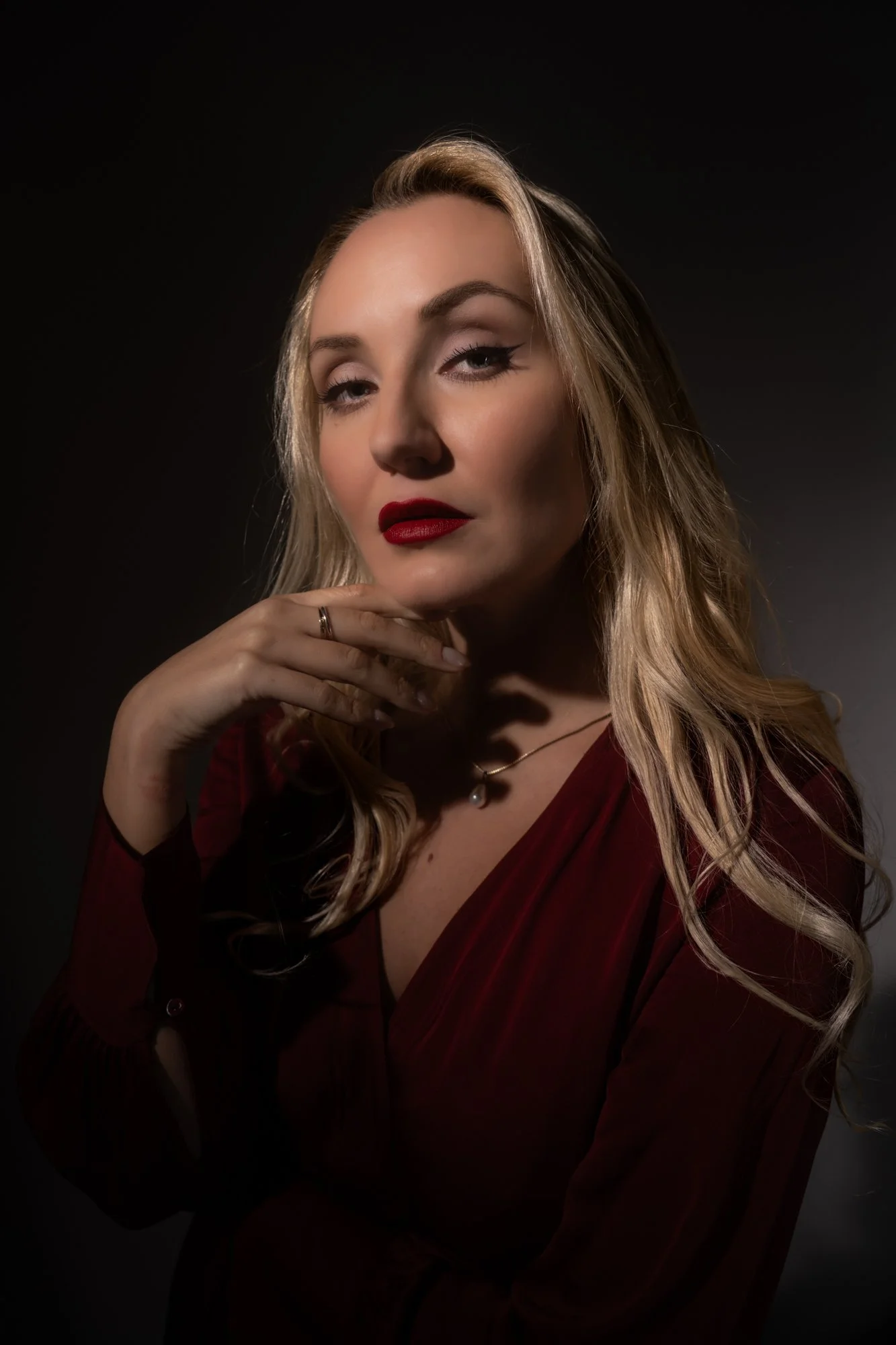 A portrait of a woman with blonde hair, red lipstick, and a red dress, against a dark background.