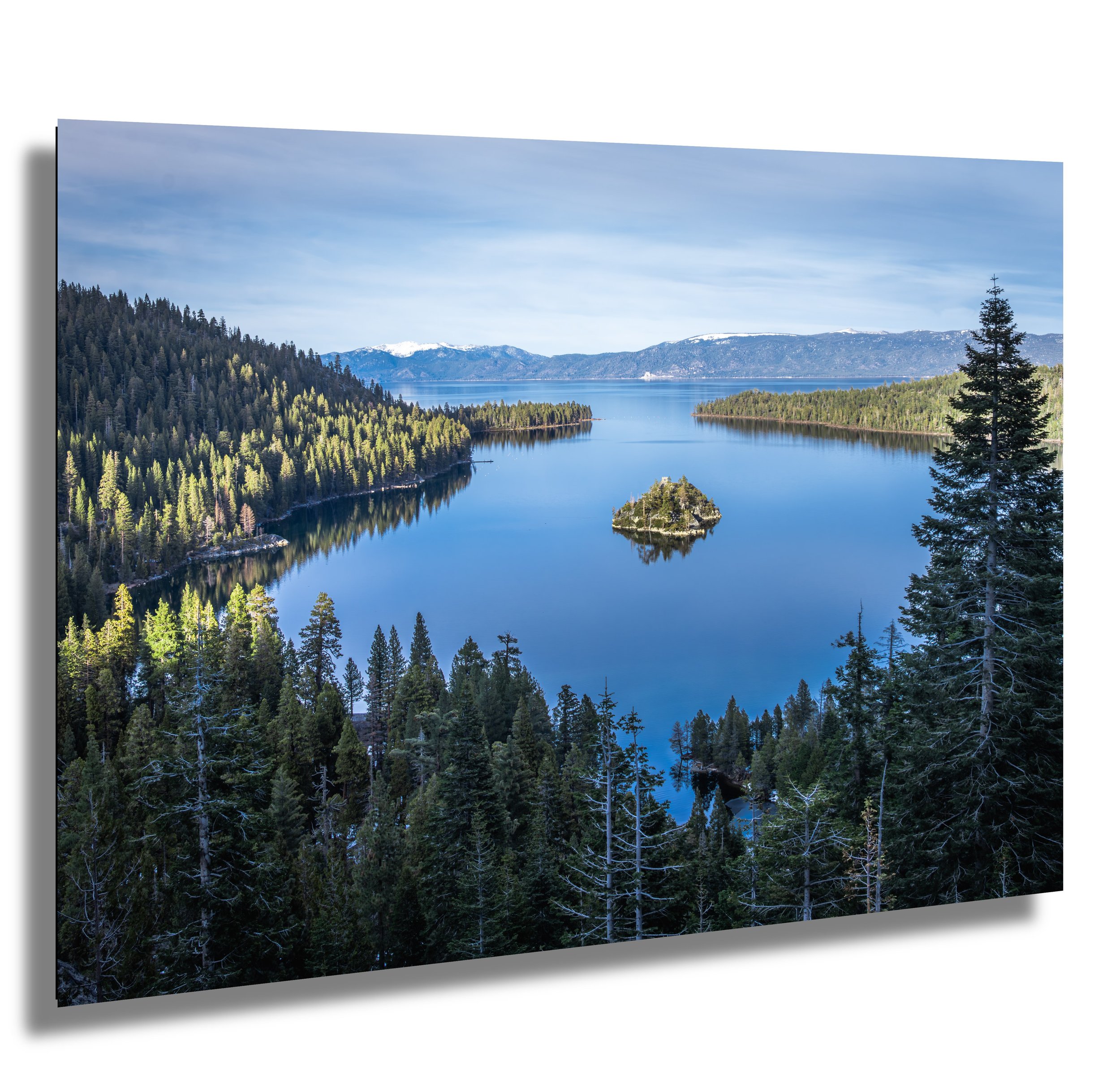 A scenic view of a river or lake surrounded by dense evergreen forests with mountains in the distance under a partly cloudy sky.