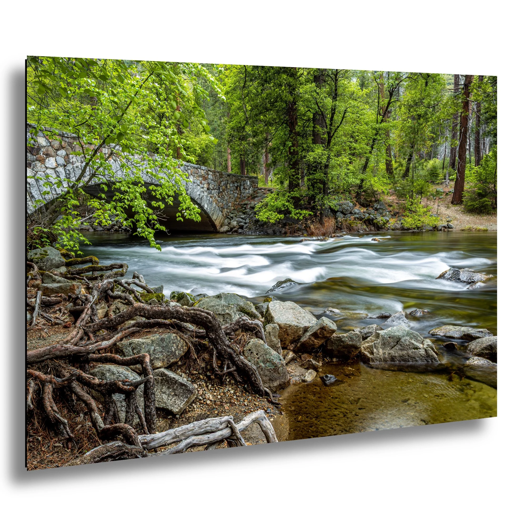 A scenic river flowing through a forest with a stone bridge and rocks along the shore.