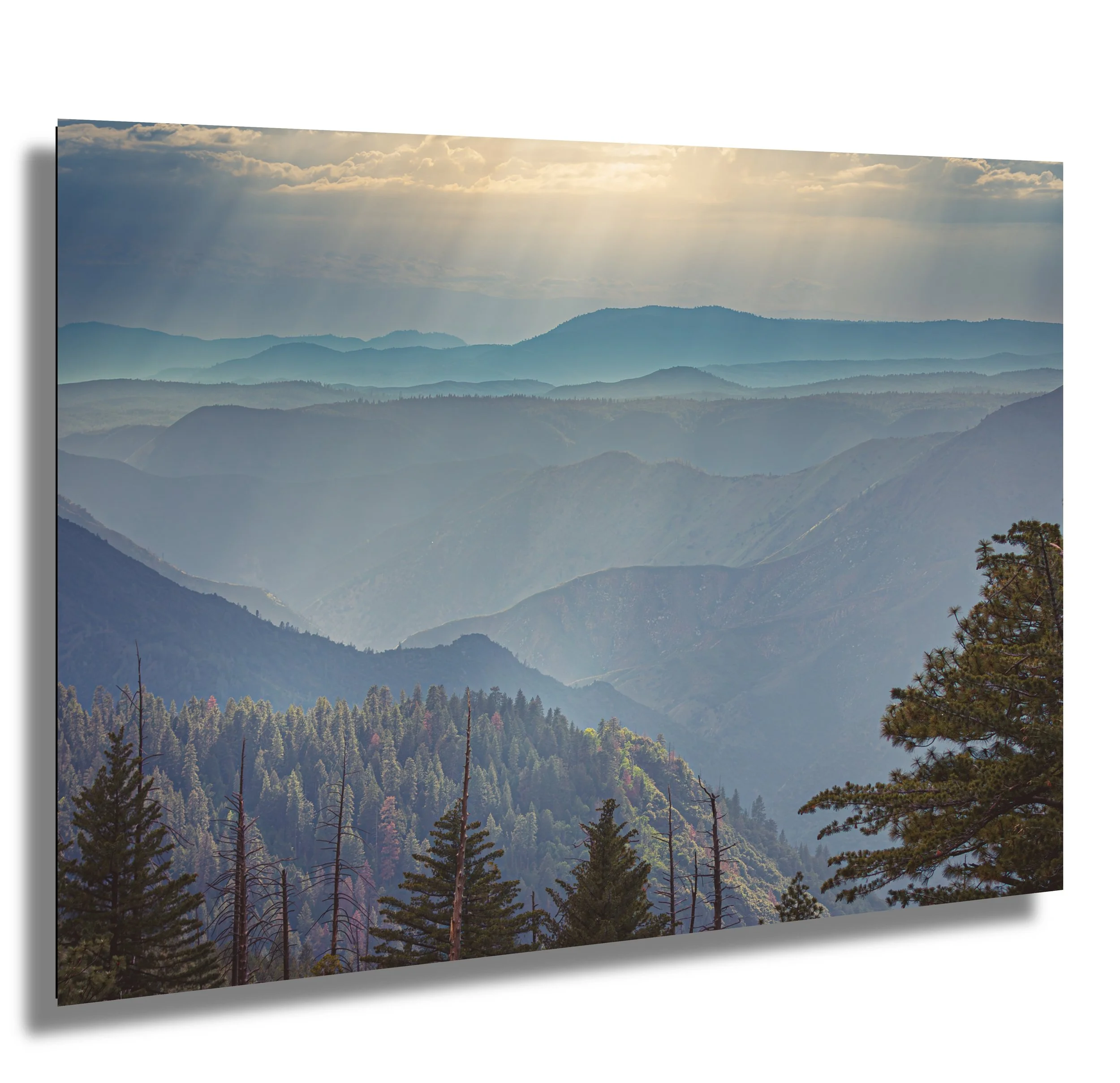 Scenic view of layered blue mountains under partly cloudy sky with sunlight breaking through clouds.
