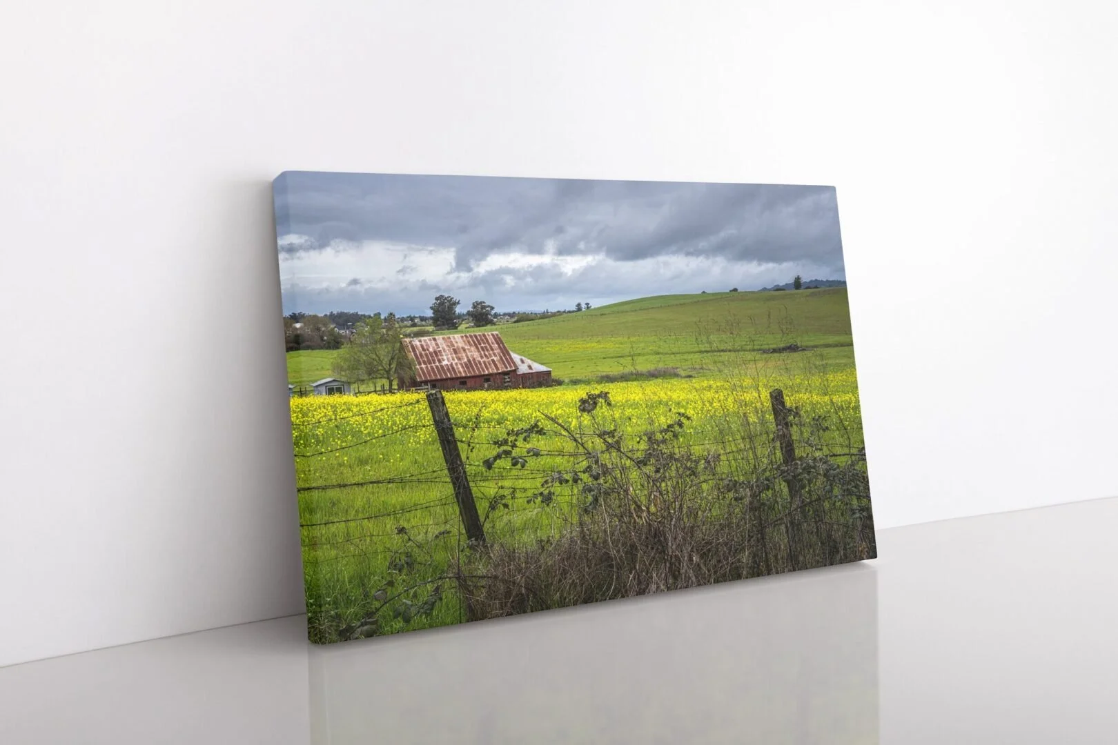 A landscape painting of a rural countryside with green rolling hills, a rusted metal roof barn, a fence, and cloudy sky.