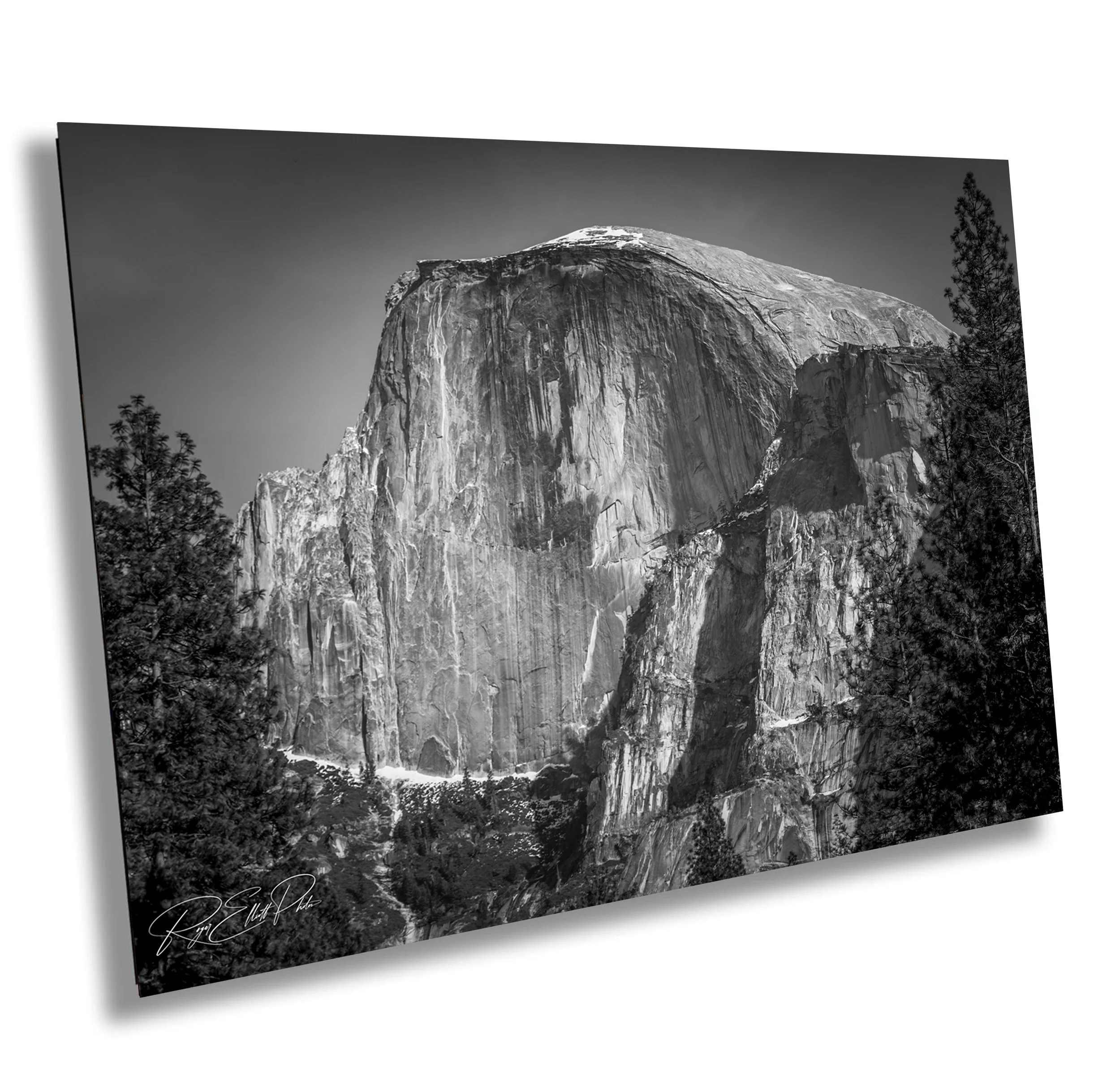 Black and white photograph of a large granite mountain with trees at the base and a clear sky above.