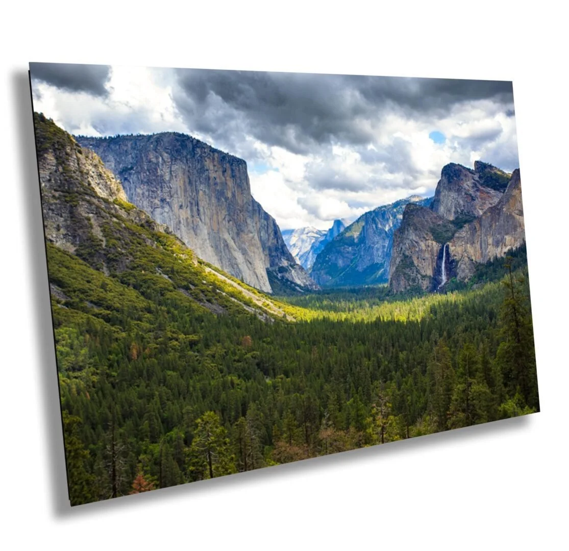 Scenic view of a lush green forest in a valley with towering cliffs on either side and a waterfall in the distance under a cloudy sky.