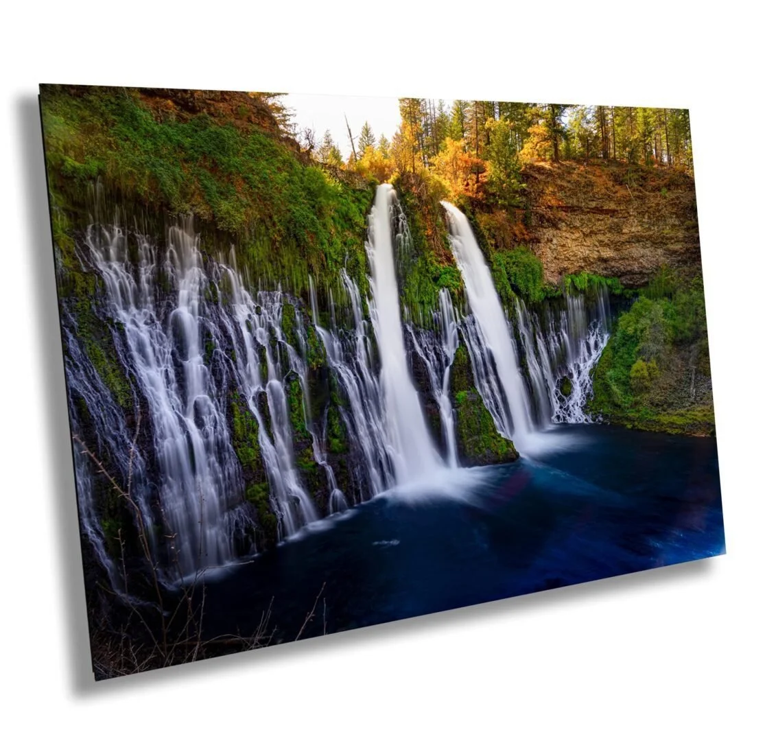 Waterfalls flowing over moss-covered rocks in a forest with trees showing autumn colors.