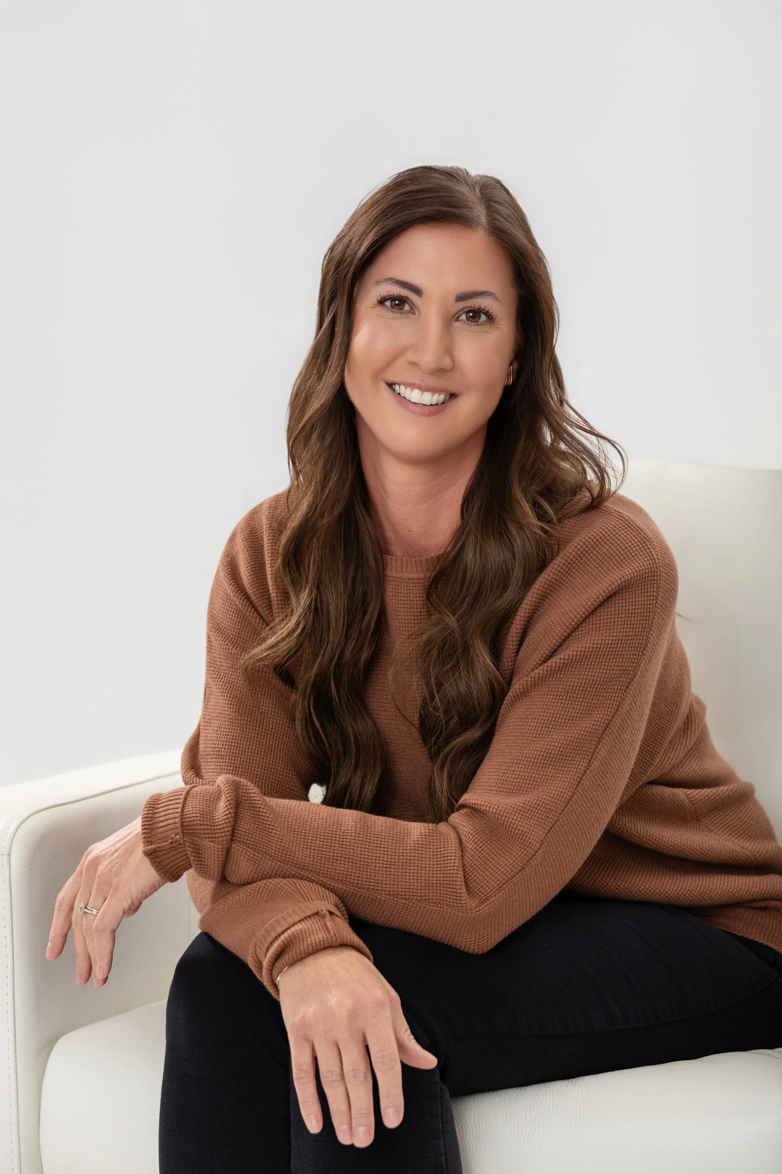 Color portrait of a woman with long wavy hair, sitting and smiling, with arms crossed