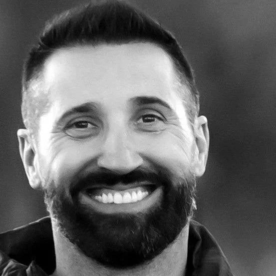 A smiling man with a beard and short hair, in black and white.
