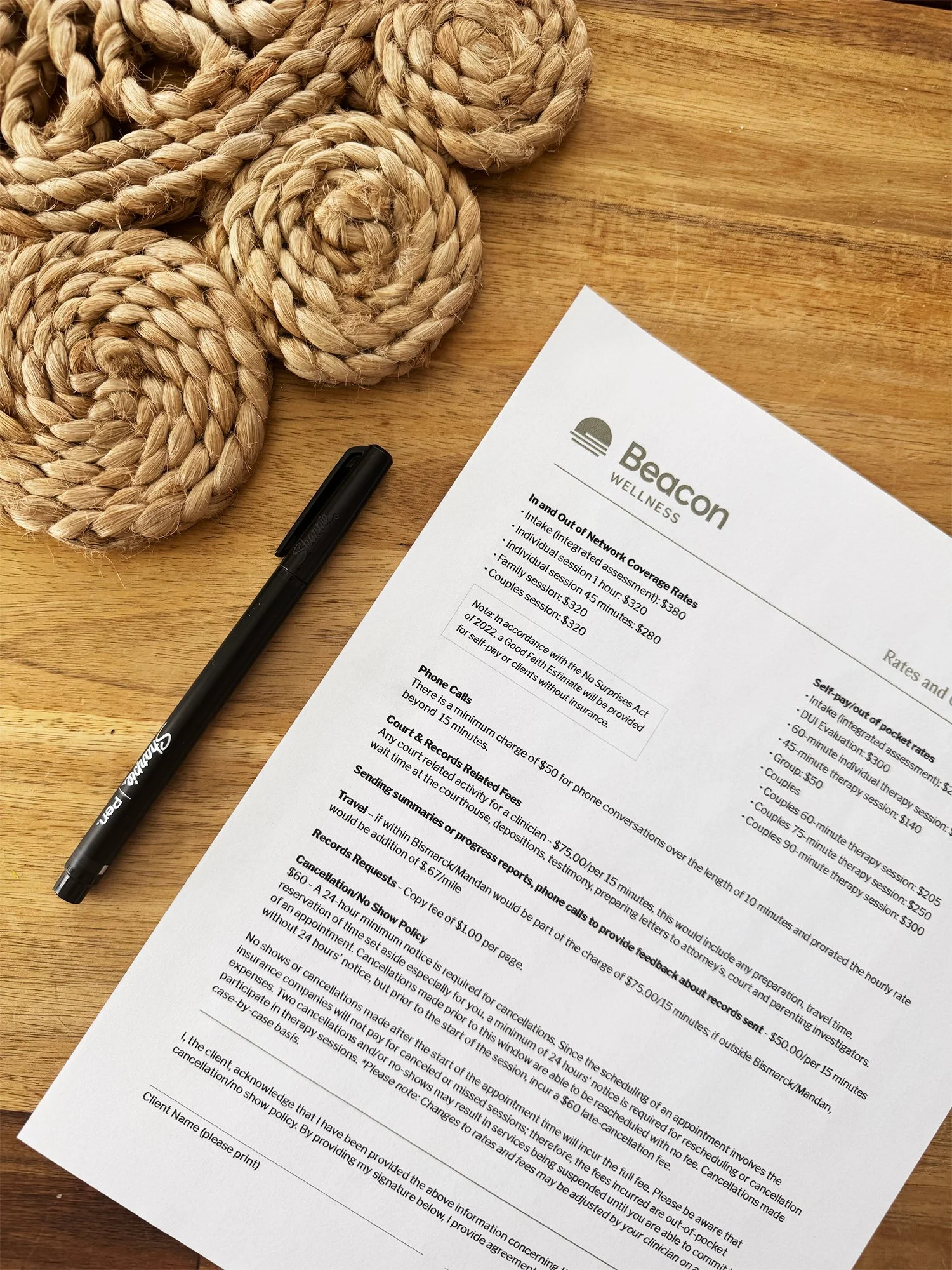 A wooden table with a black marker, a printed document titled 'Beacon Wellness' with various text and rates, and thick braided rope coiled on the top-left side.