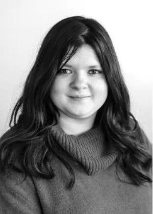 Black and white portrait of a woman with long, dark hair, wearing a sweater and smiling.