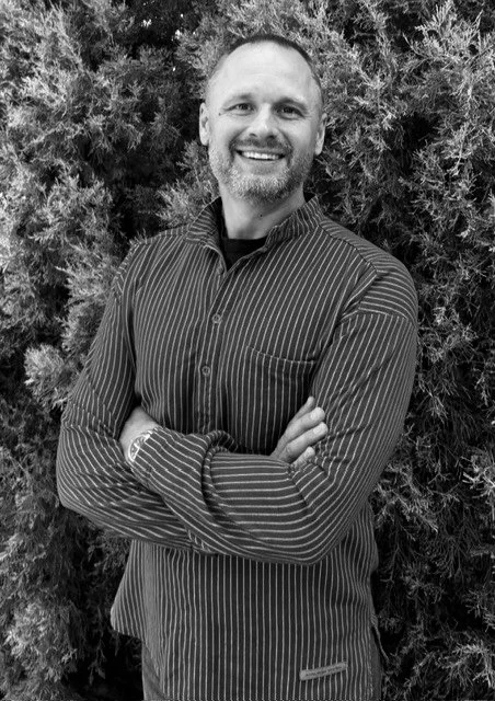 Smiling man in striped shirt, standing in front of trees