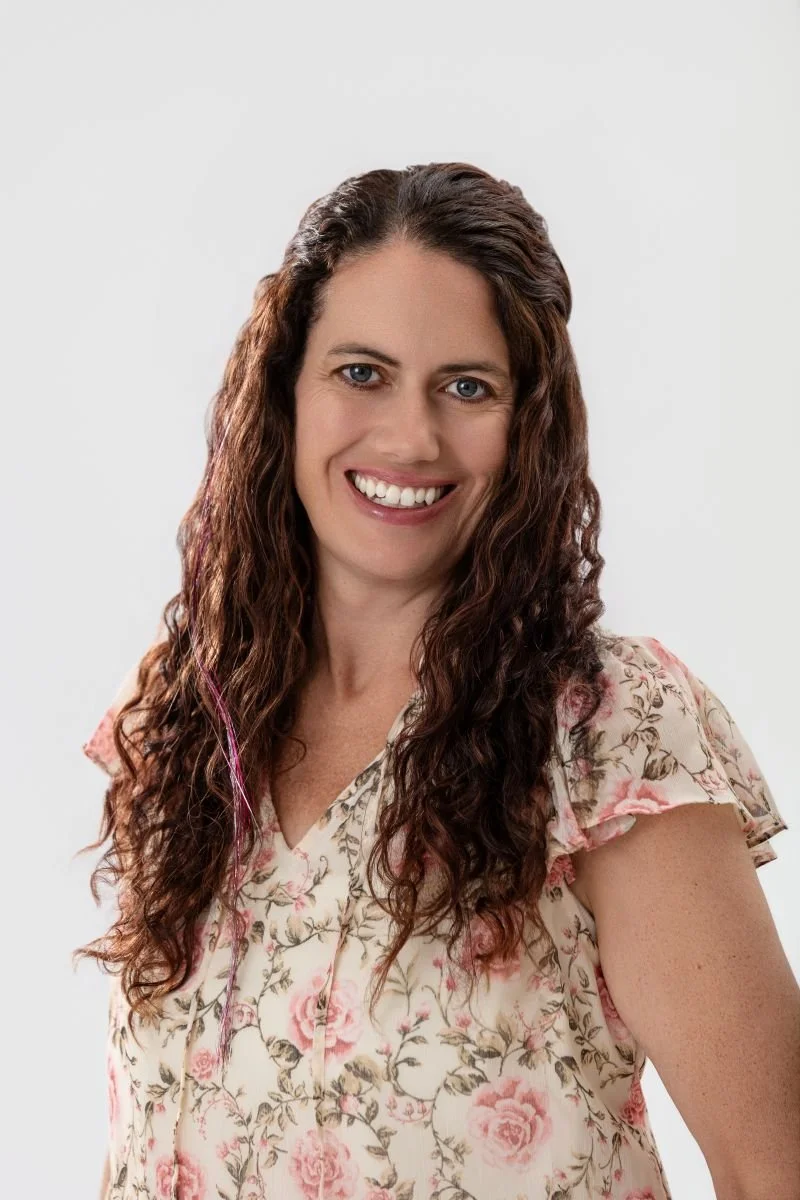Color portrait of a woman with long, wavy hair and light-colored eyes, wearing a floral blouse and smiling.