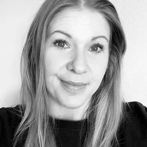 Portrait of a woman with long hair and a nose piercing, smiling slightly, in black and white.