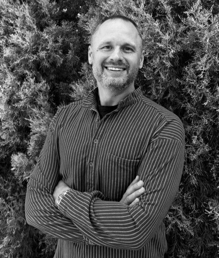 Black and white photo of man smiling and standing in front of trees