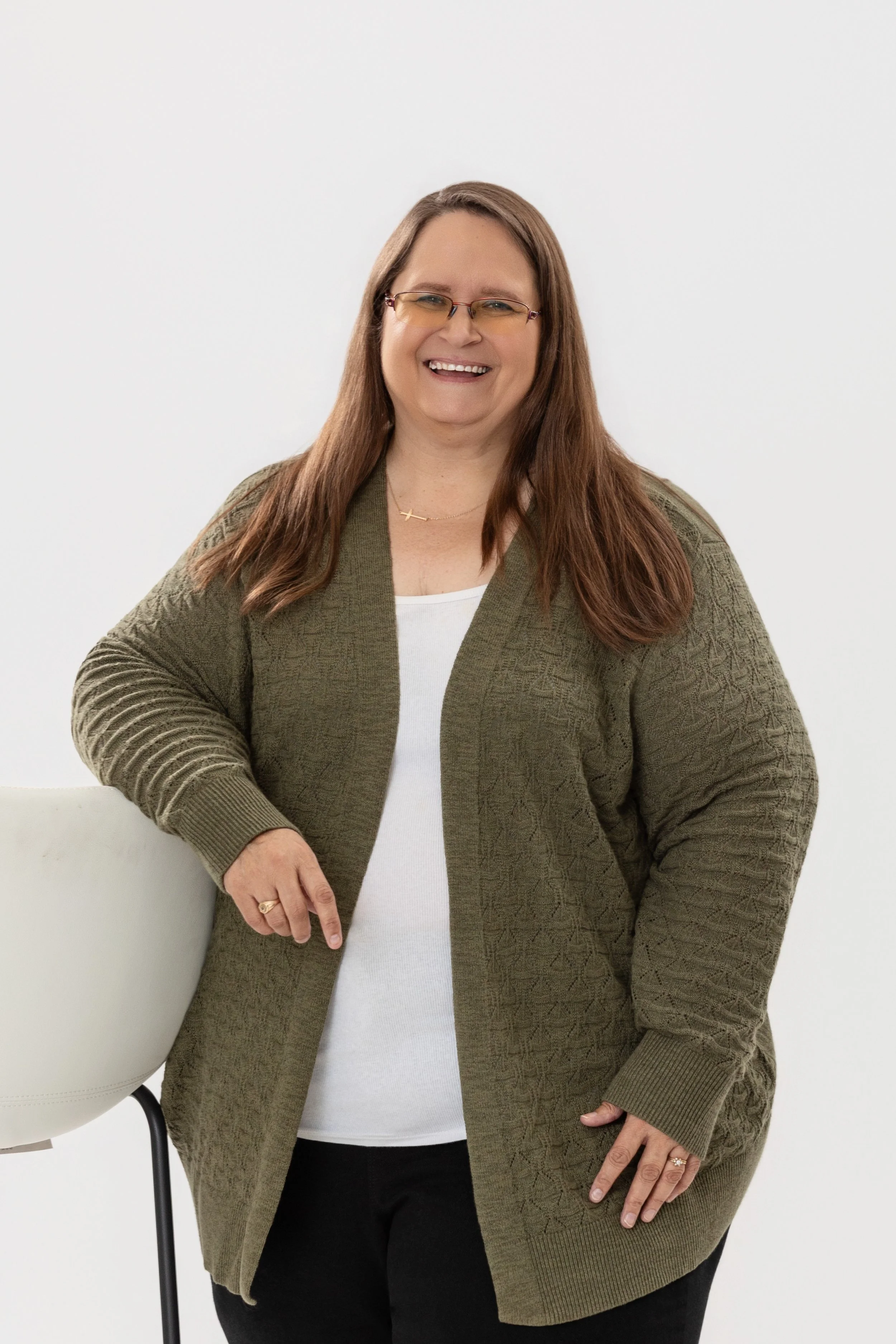 Color portrait of a smiling woman with glasses, long hair, wearing a textured cardigan and standing.