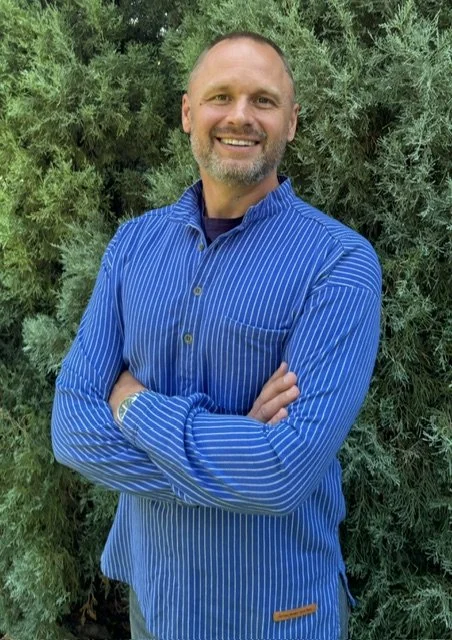 Color portrait of Man standing and smiling in front of trees