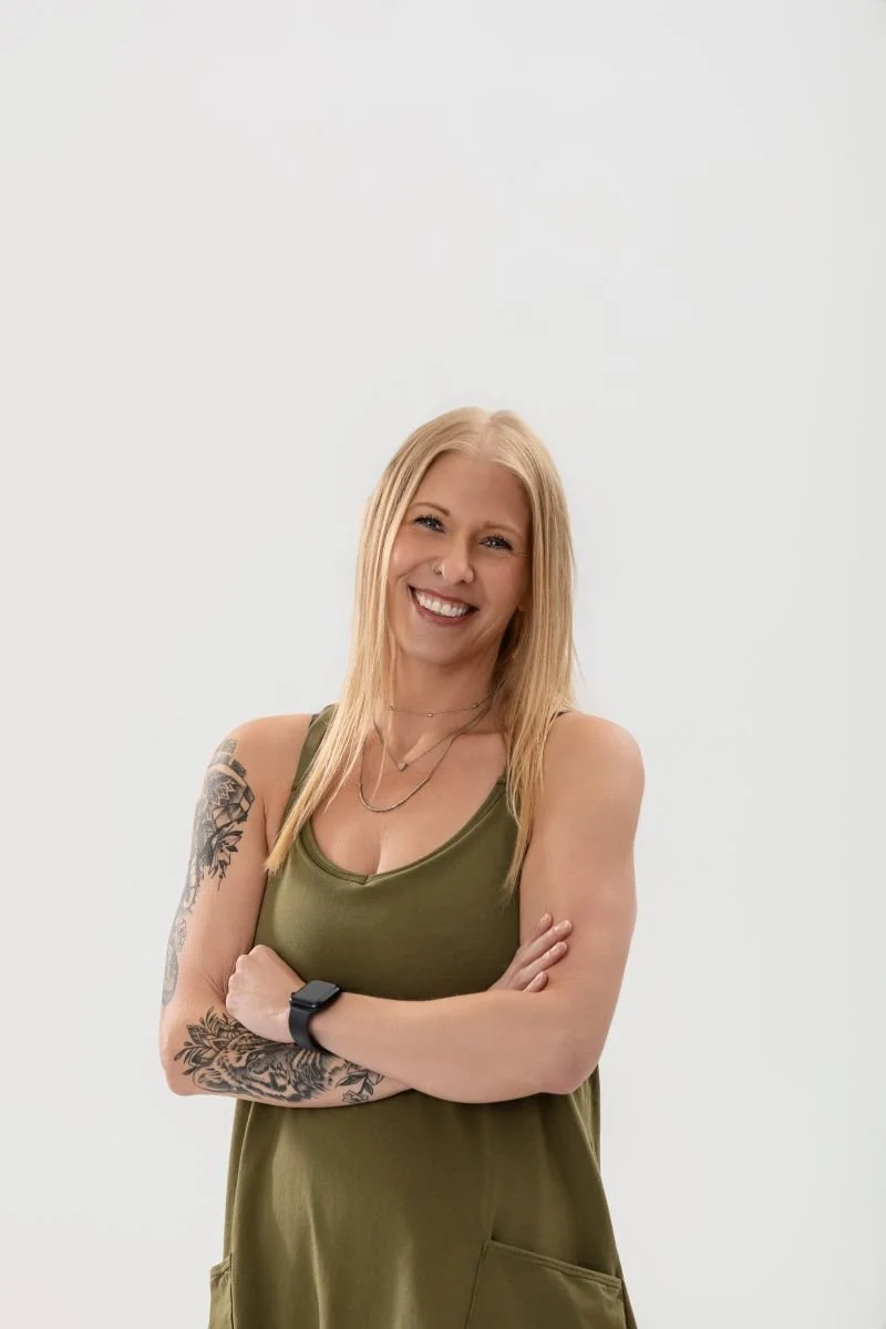 Color portrait of smiling woman with tattoos, arms crossed, wearing a dress against white background