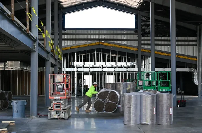 Construction worker moving large rolls of insulation in a building under construction.