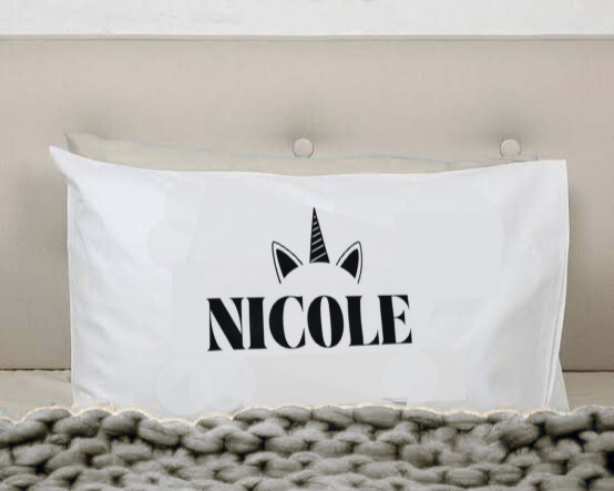 A white pillow with the name 'NICOLE' and a unicorn horn and ears design.