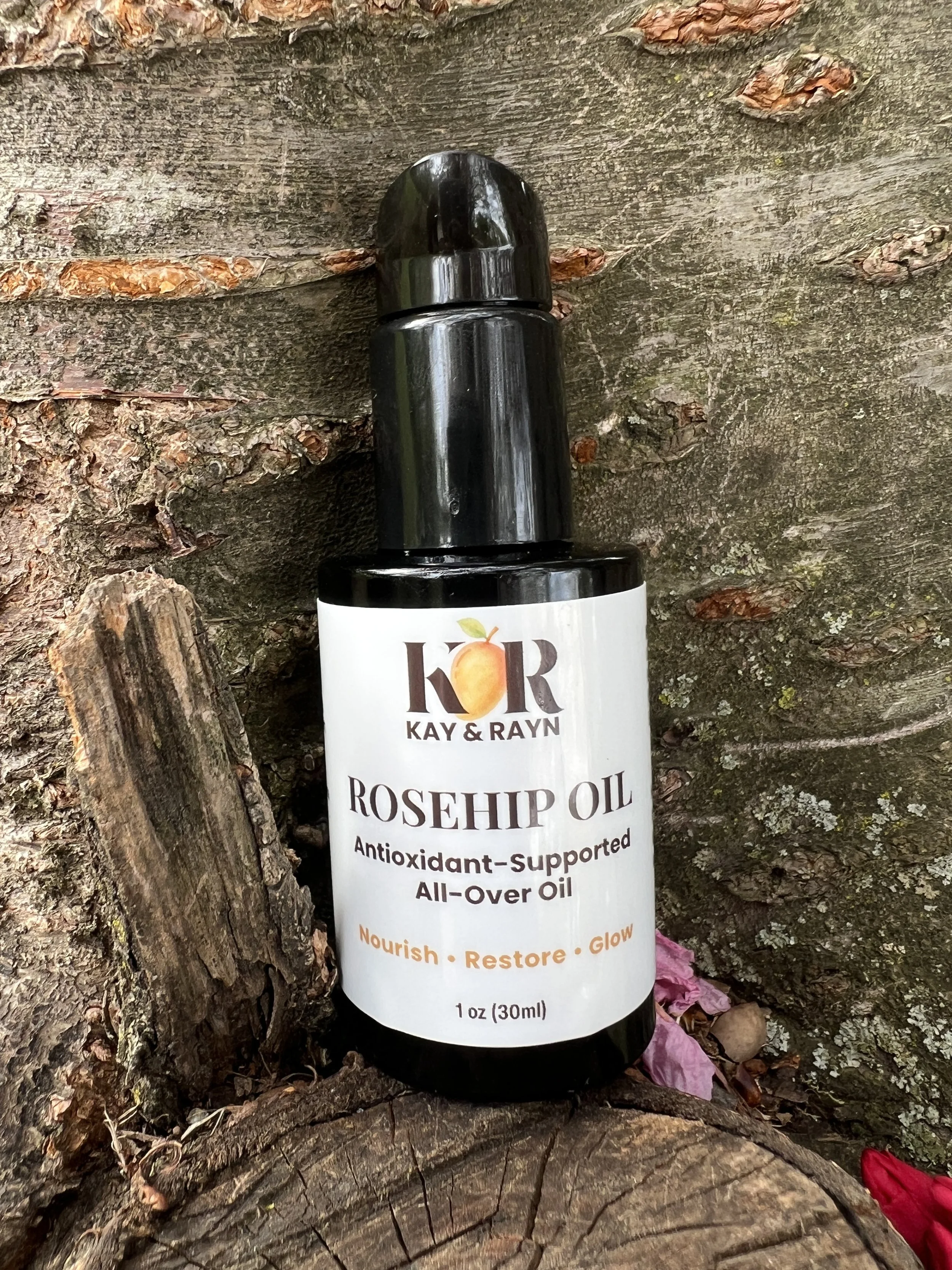 A bottle of rosehip oil resting against a rough, textured, brown tree trunk with small pieces of bark and wood nearby.