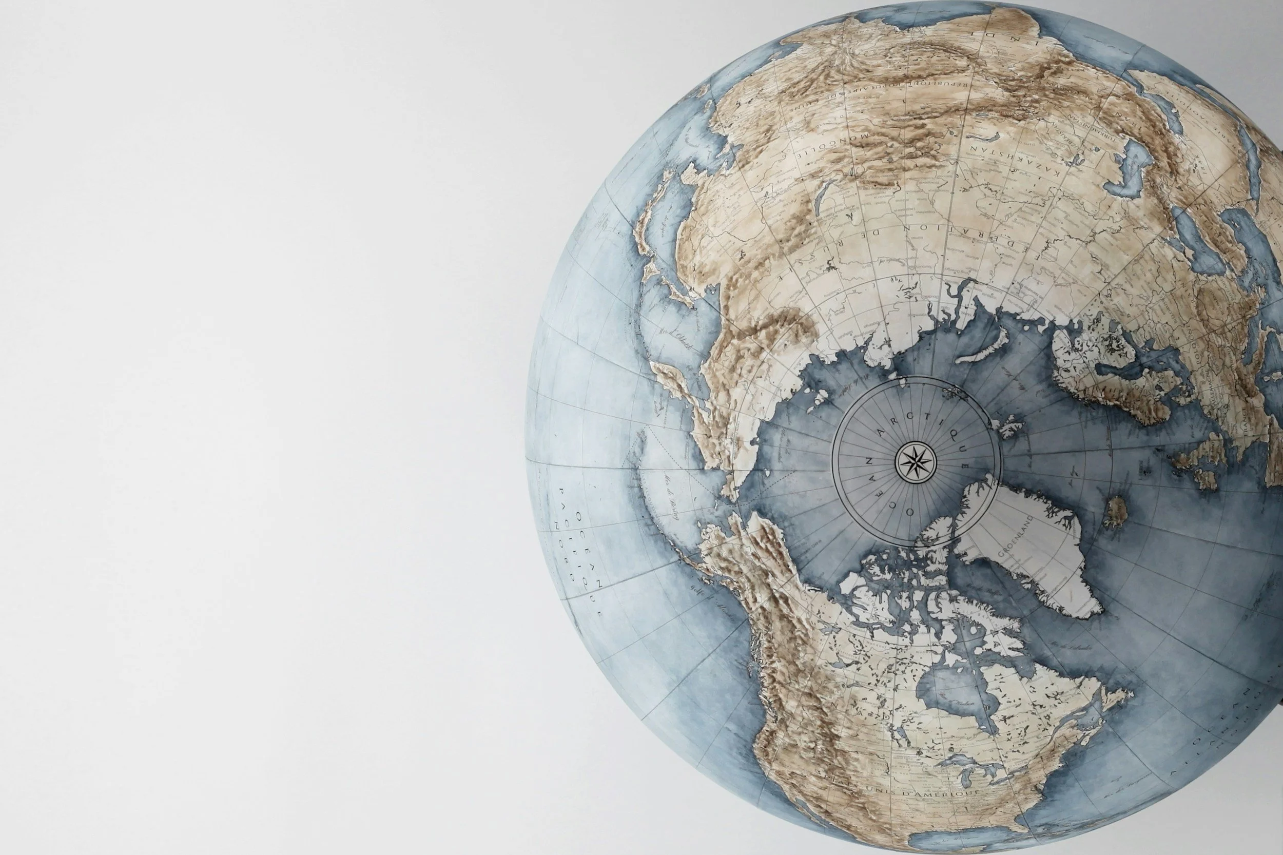 Globo terráqueo antiguo con mapa en tonos de sepia y azul, mostrando los continentes y océanos del hemisferio norte y sur, con líneas de latitud y longitud y una rosa de los vientos en el centro.