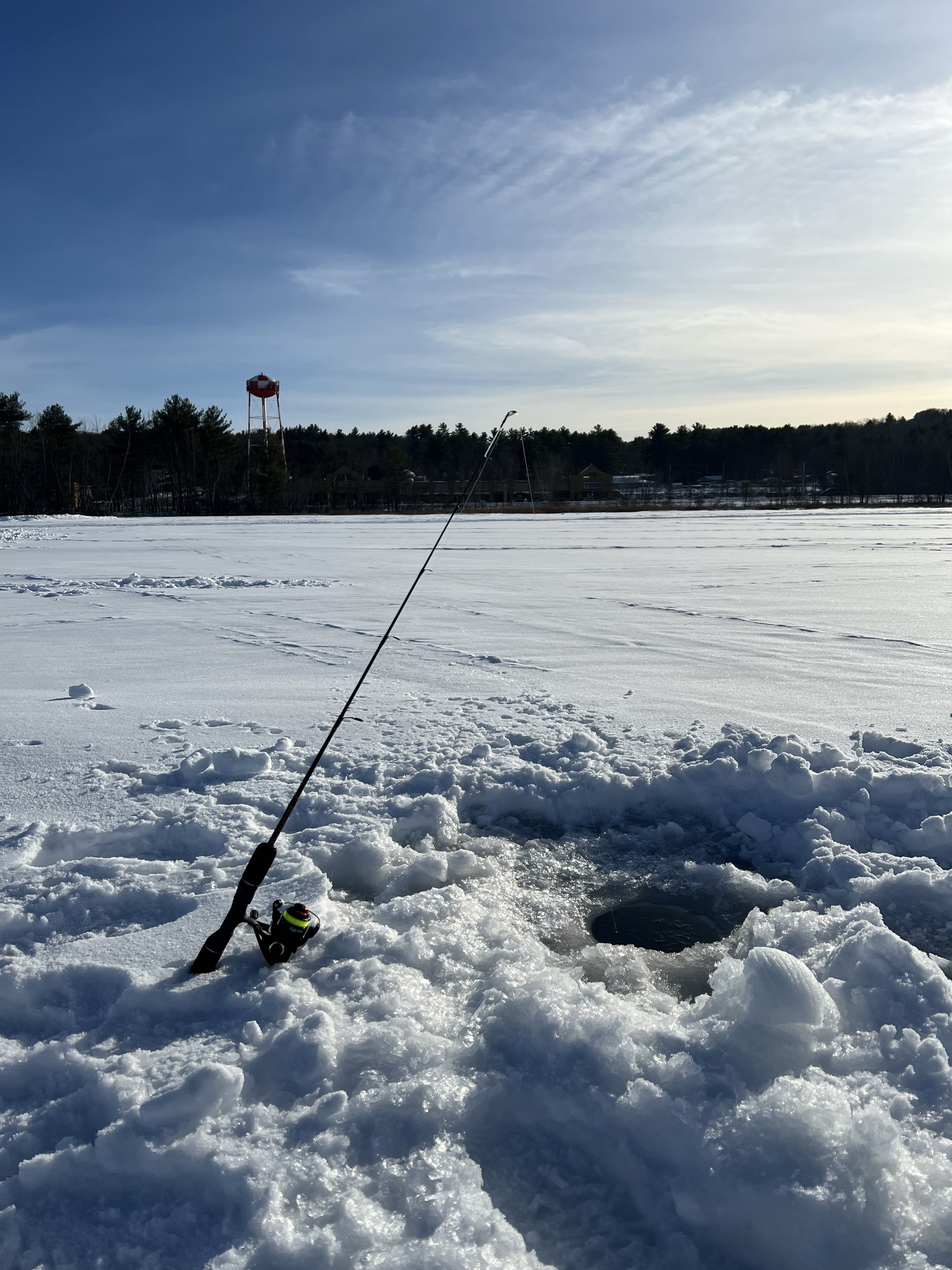 Ice fishing scene on a snowy lake with a fishing rod and a small hole in the ice.