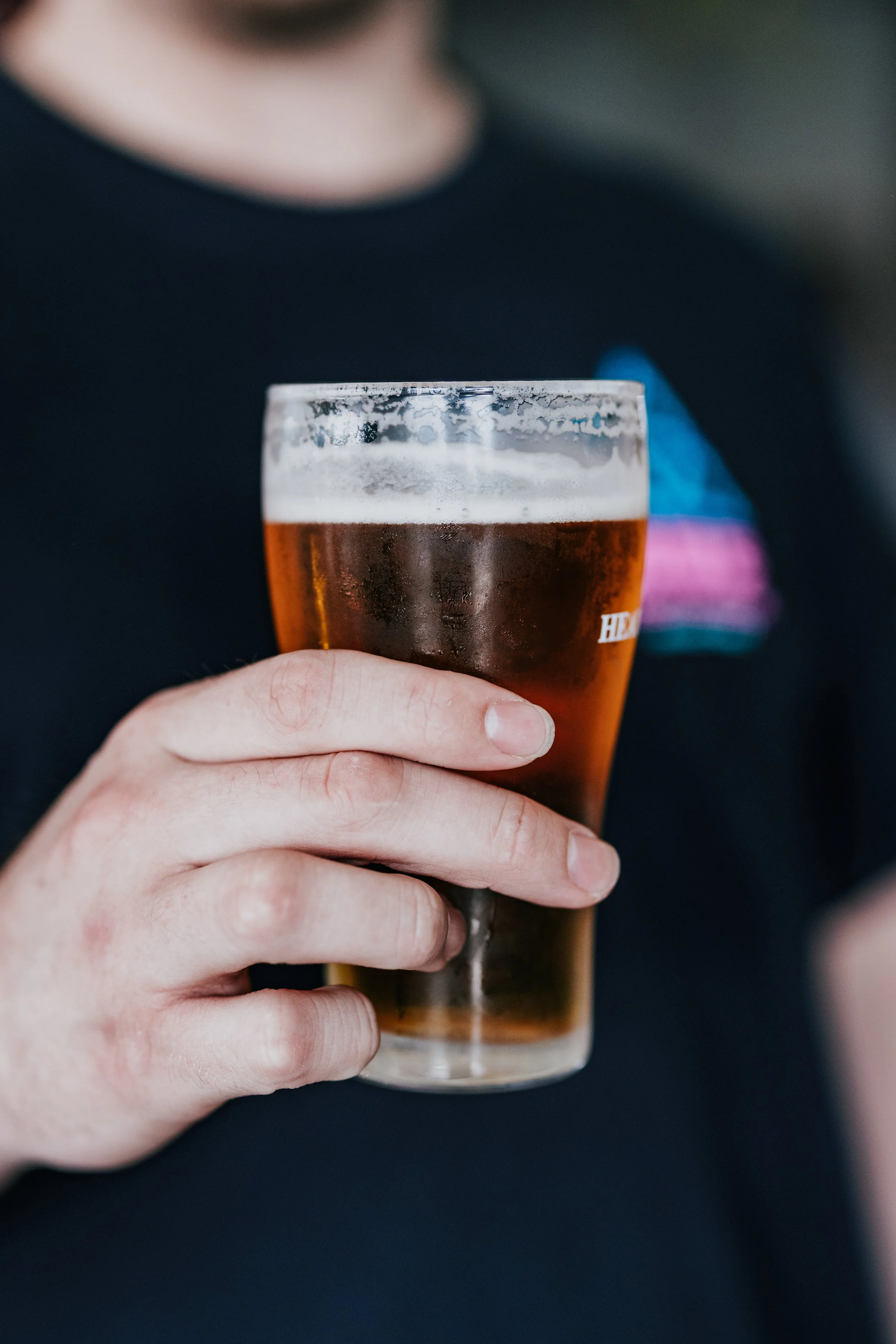 A person holding a glass of amber beer with a foamy head.