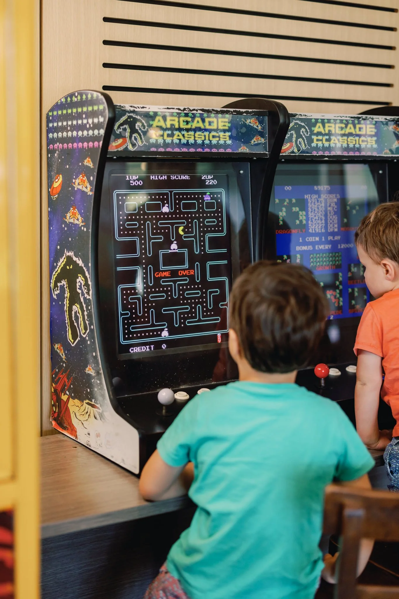 Two children playing Pac-Man arcade game with the screen showing a game over message.