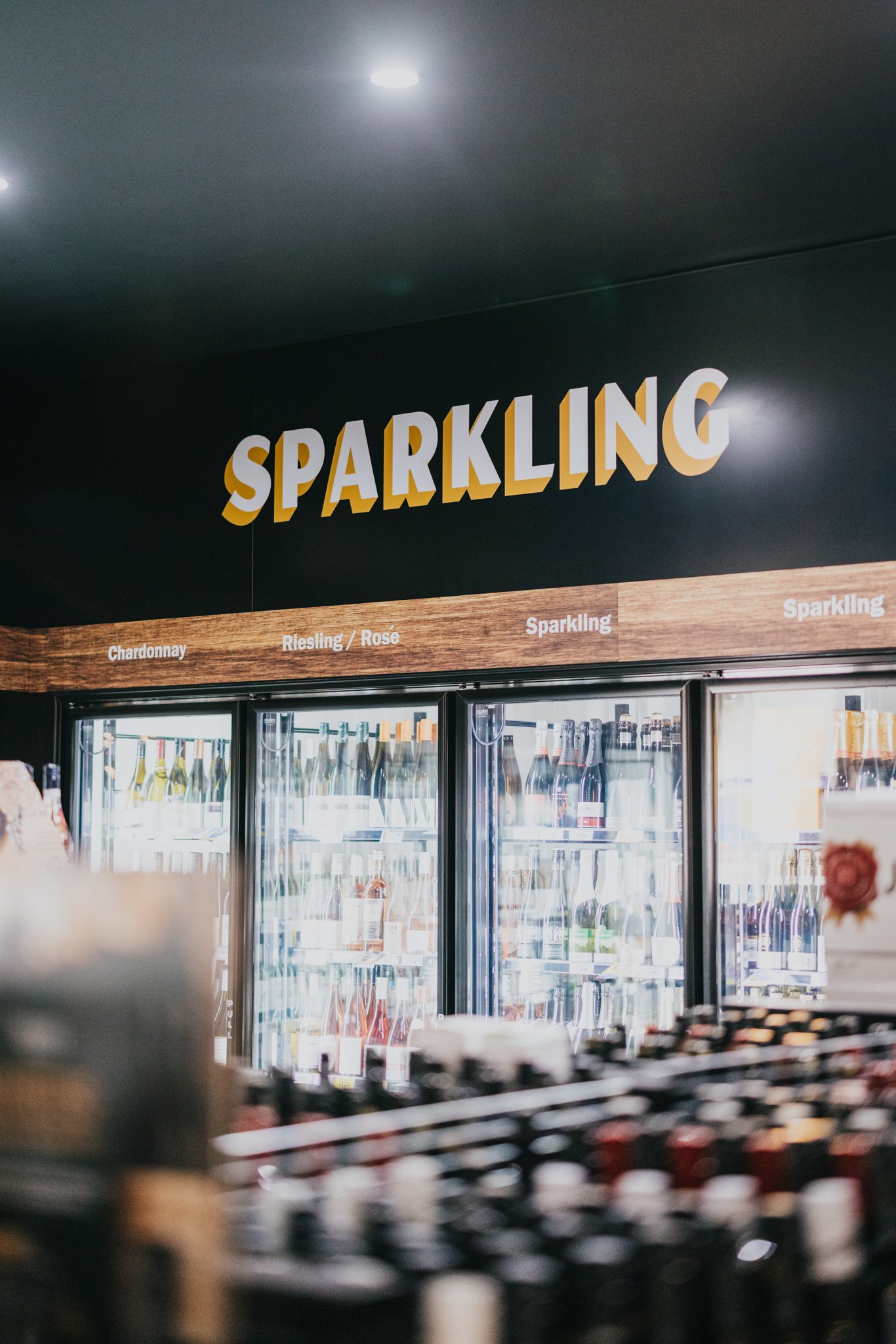 A store section labeled 'SPARKLING' displaying bottles of sparkling wine or champagne in refrigerated display case.