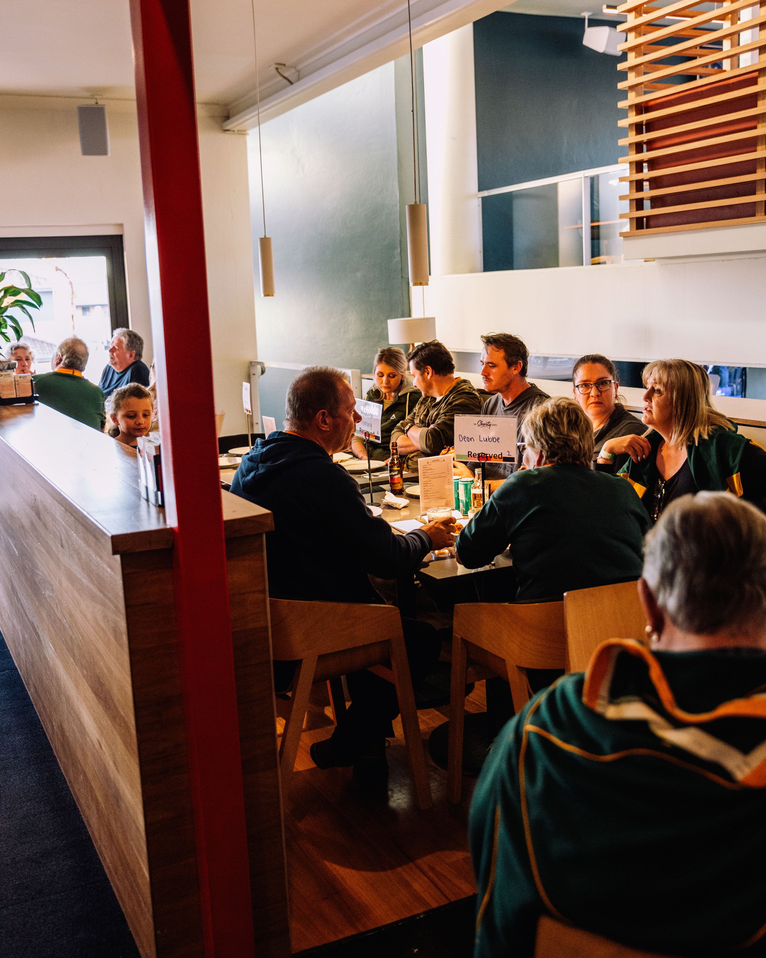 People sitting at tables inside a restaurant or cafe, engaged in conversation and enjoying meals, with some facing away from the camera.