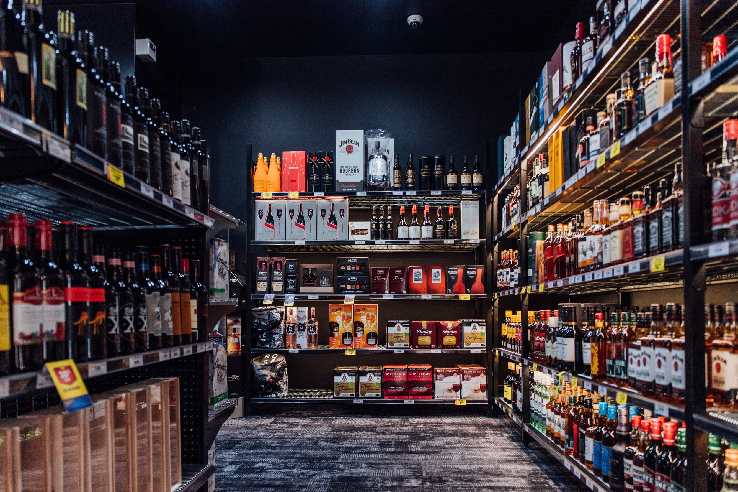 Interior of a liquor store aisle with shelves stocked with various bottles of alcohol, including whiskey, bourbon, and other spirits on black shelves.