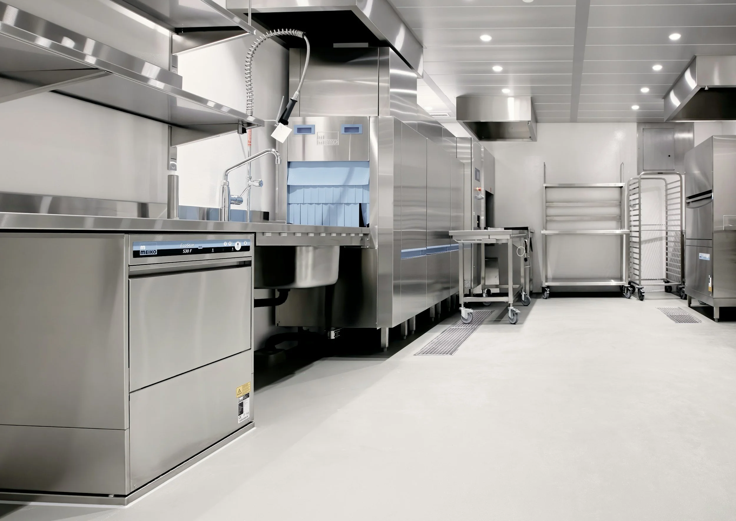 A clean, empty commercial kitchen with stainless steel appliances, sinks, and carts.