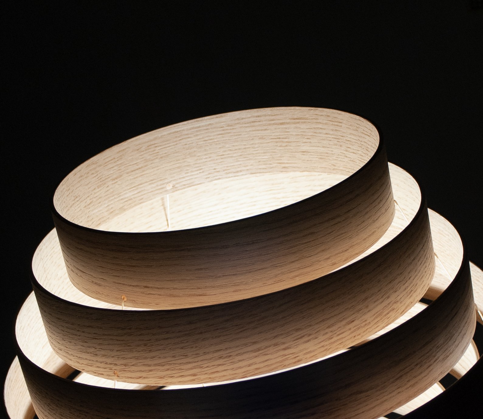 Close-up of a modern ceiling light fixture with layered circular wooden panels against a black background.