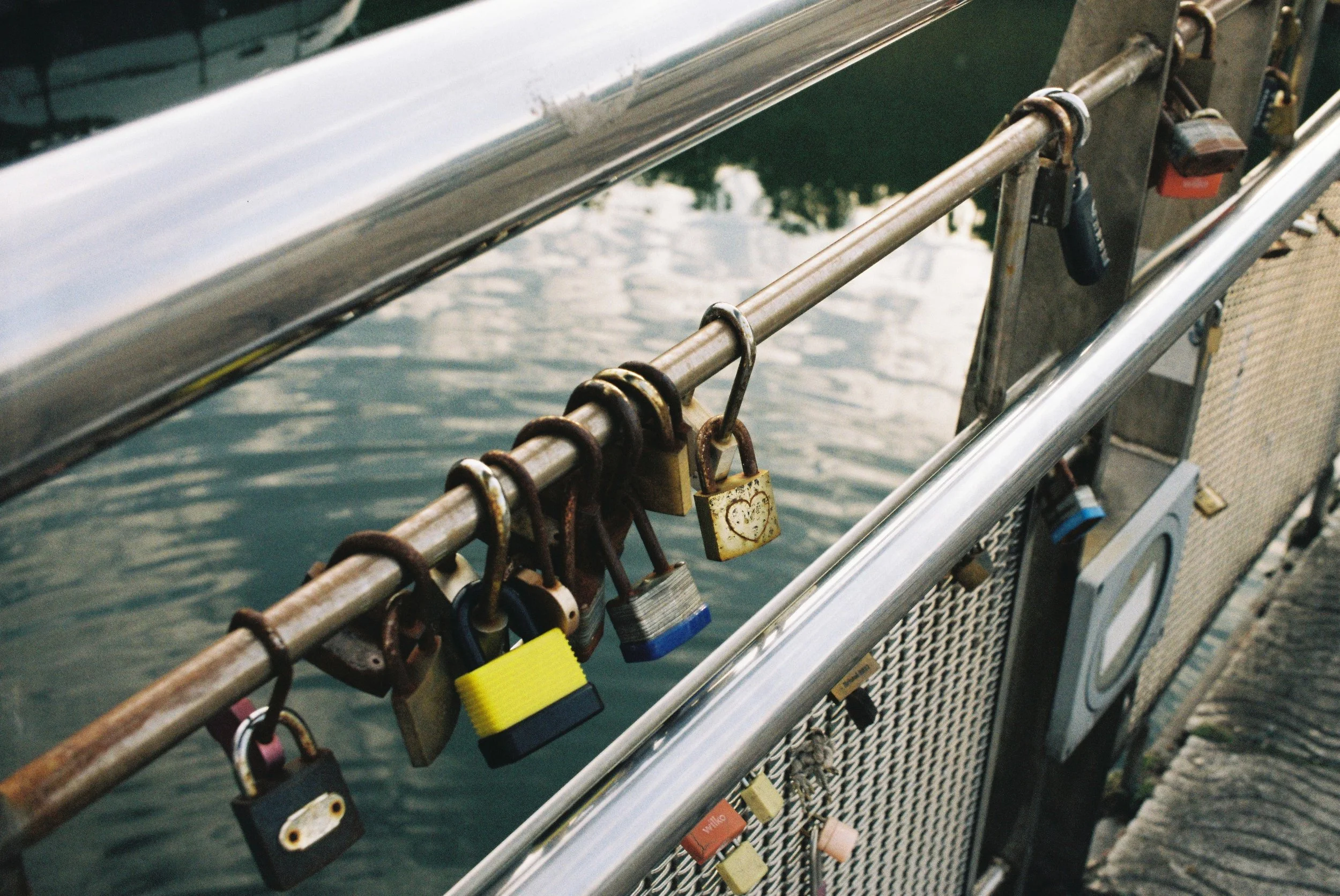 Close-up of a metal railing with numerous locks attached, overlooking a body of water.