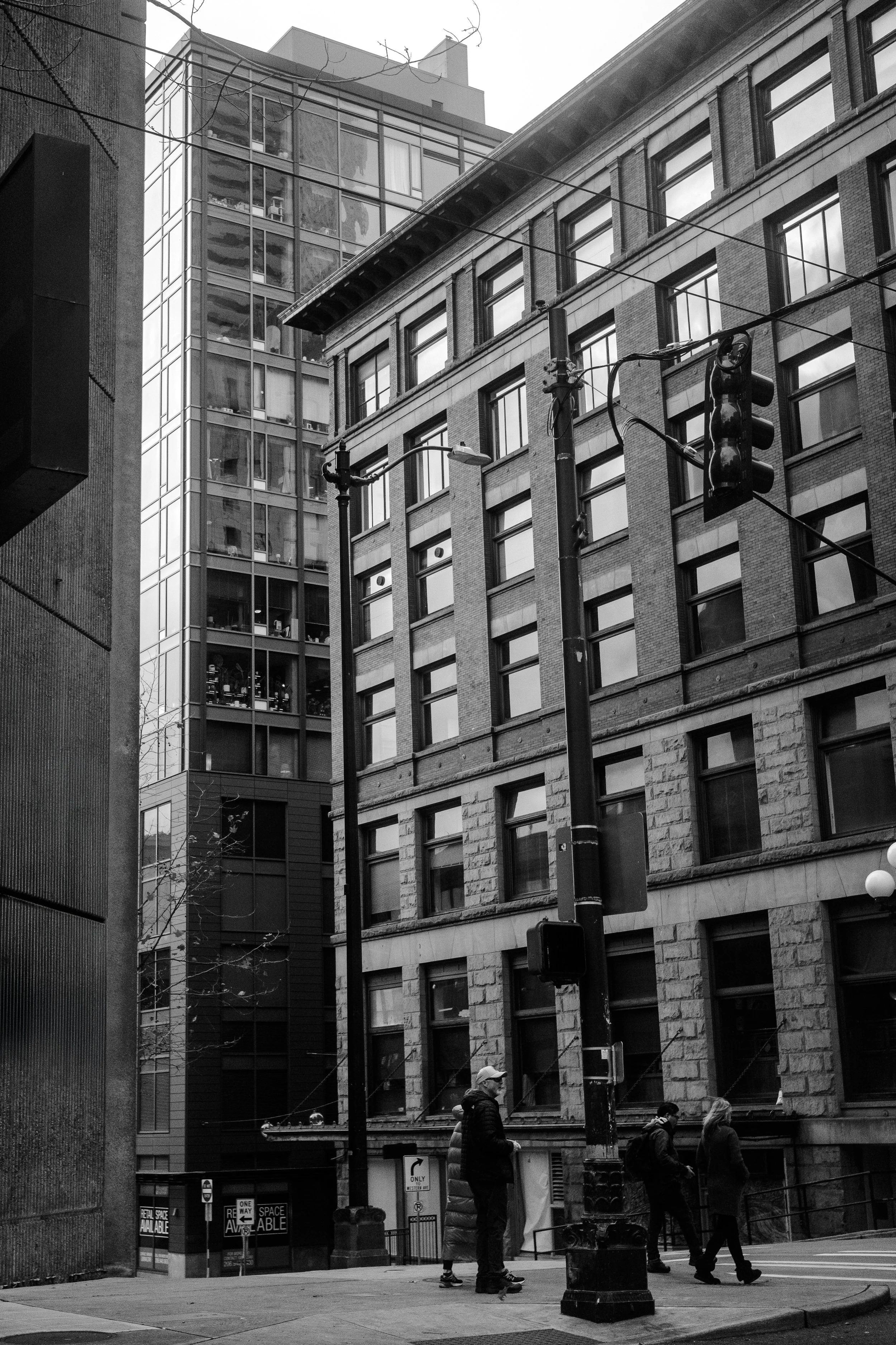 City street scene in black and white with tall buildings, traffic signal, and pedestrians crossing the street.