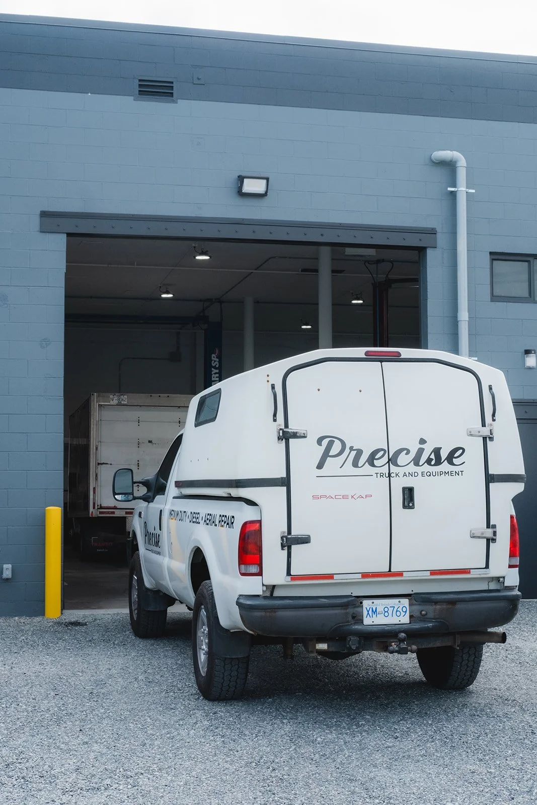 A white work van parked outside an industrial building with loading dock and garage door open.