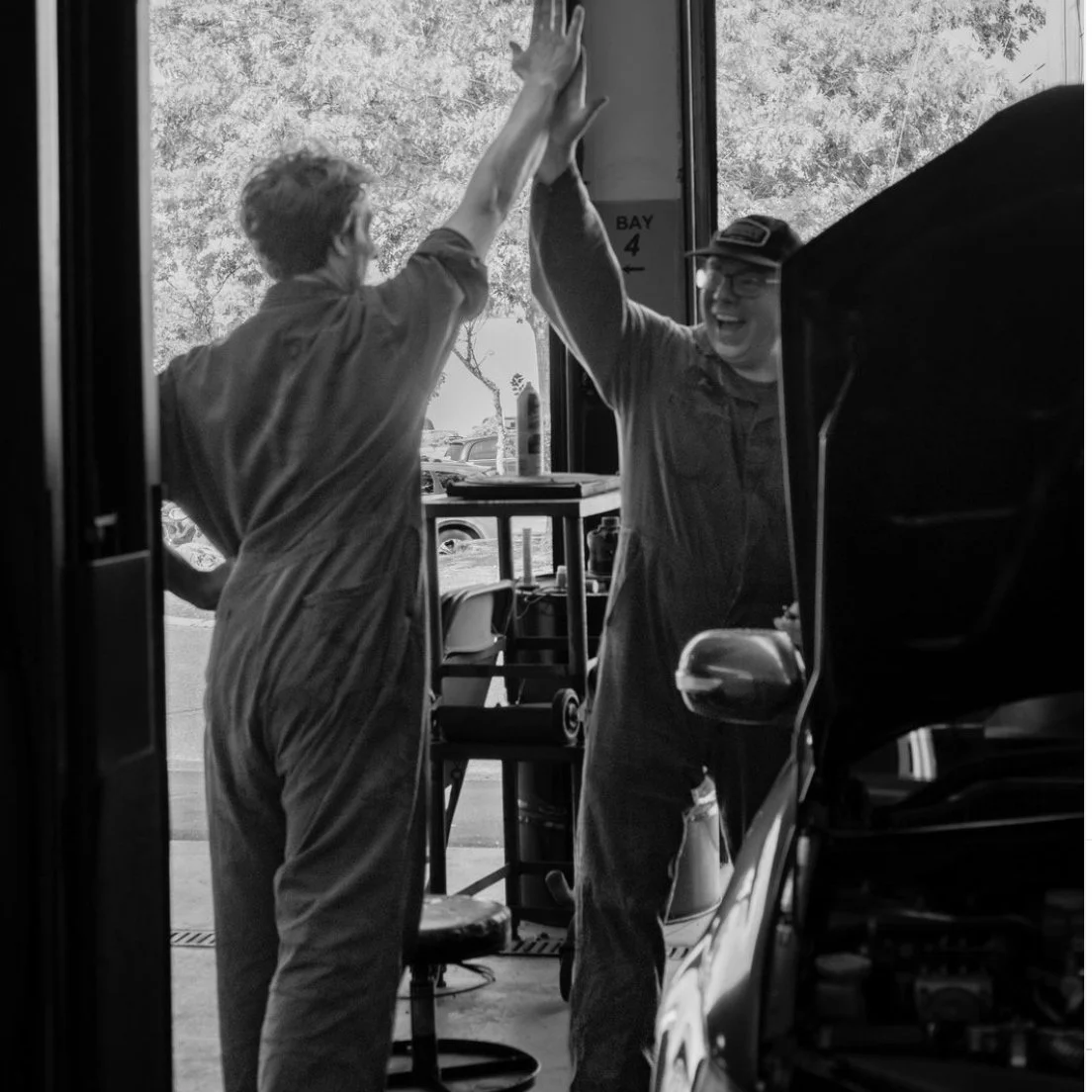 Two people in a garage giving high fives and smiling.