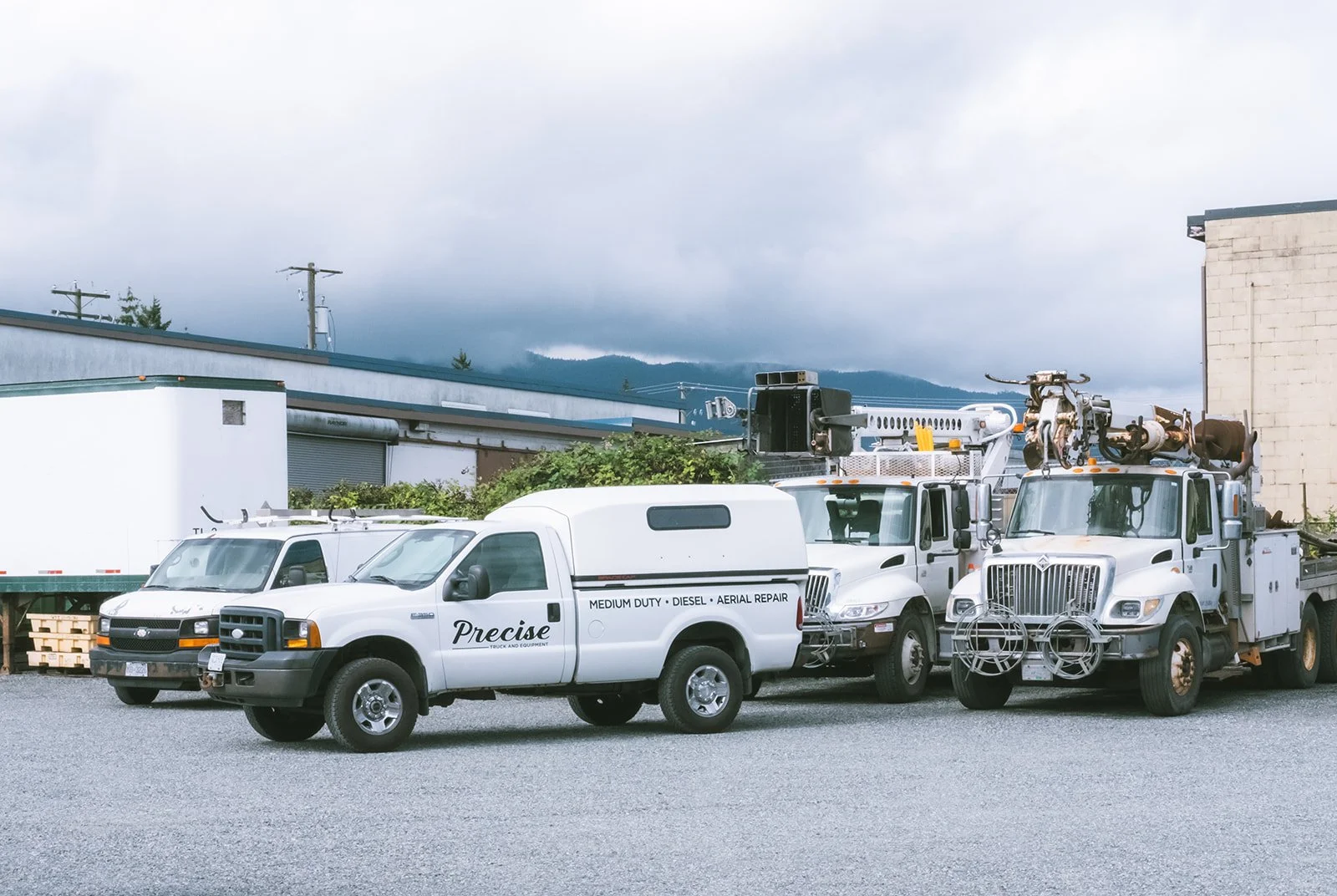Three service trucks parked outdoors, with equipment and tools, against a cloudy sky and mountain backdrop