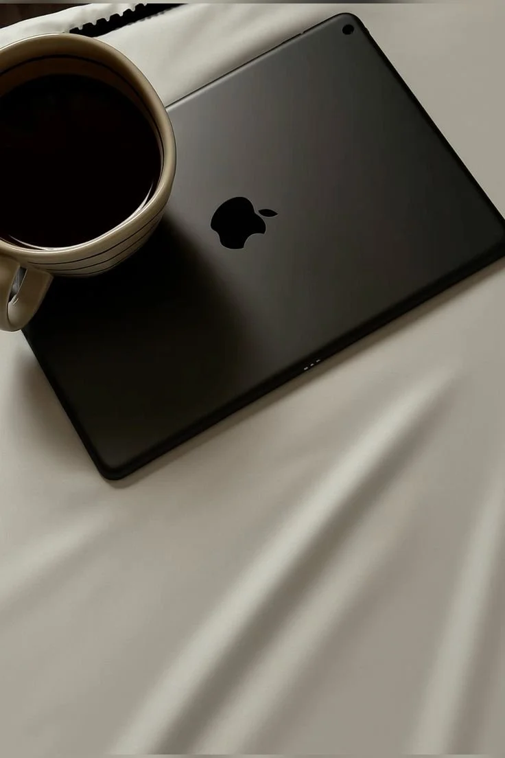 A black iPhone with a silver apple logo and a cup of black coffee on a light-colored fabric surface.