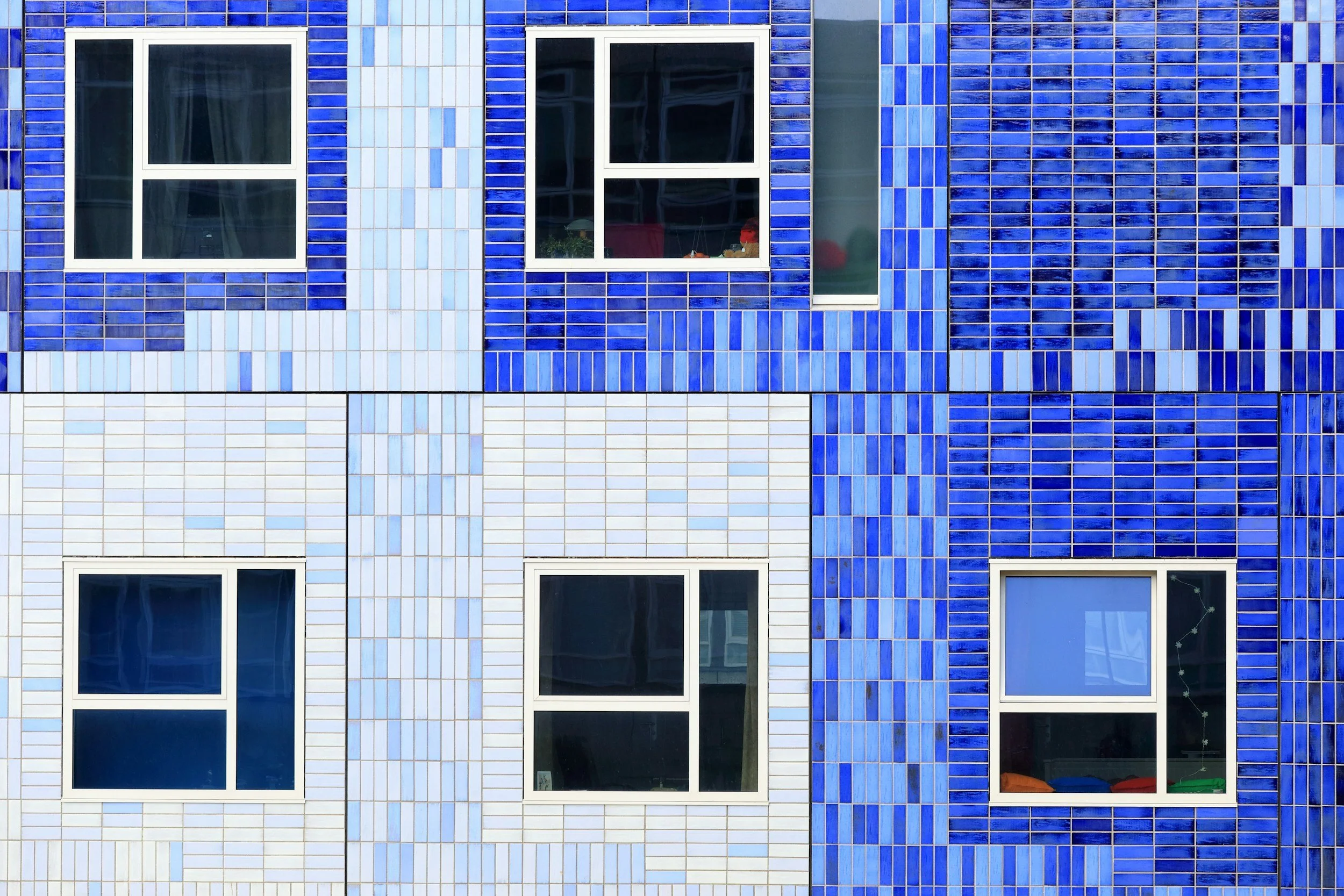 Close-up of a building's exterior wall with colorful blue and white tiles, featuring four rectangular windows with white frames.